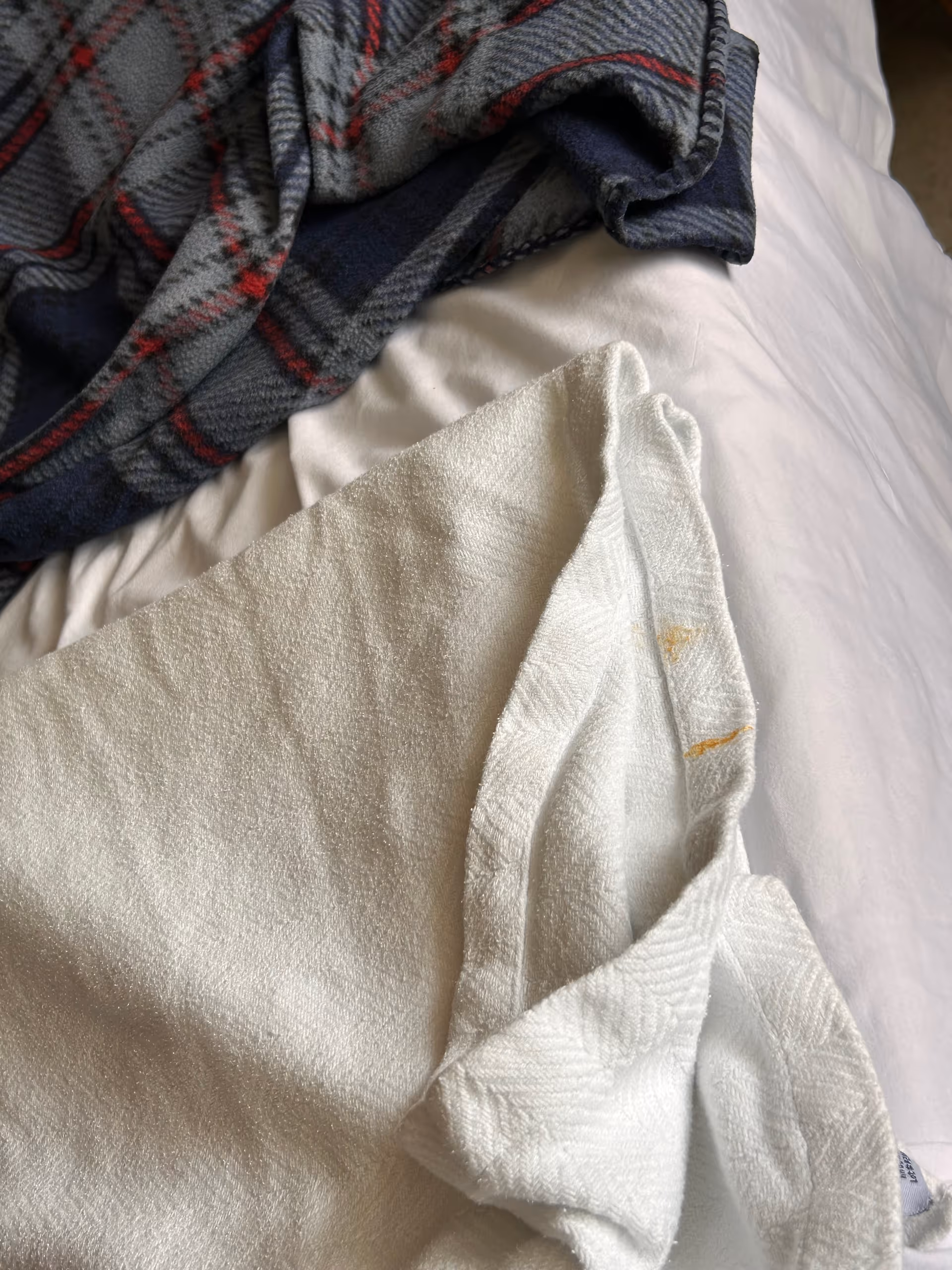 Close-up of a bed with white linens, a towel, and plaid blanket in a bedroom.