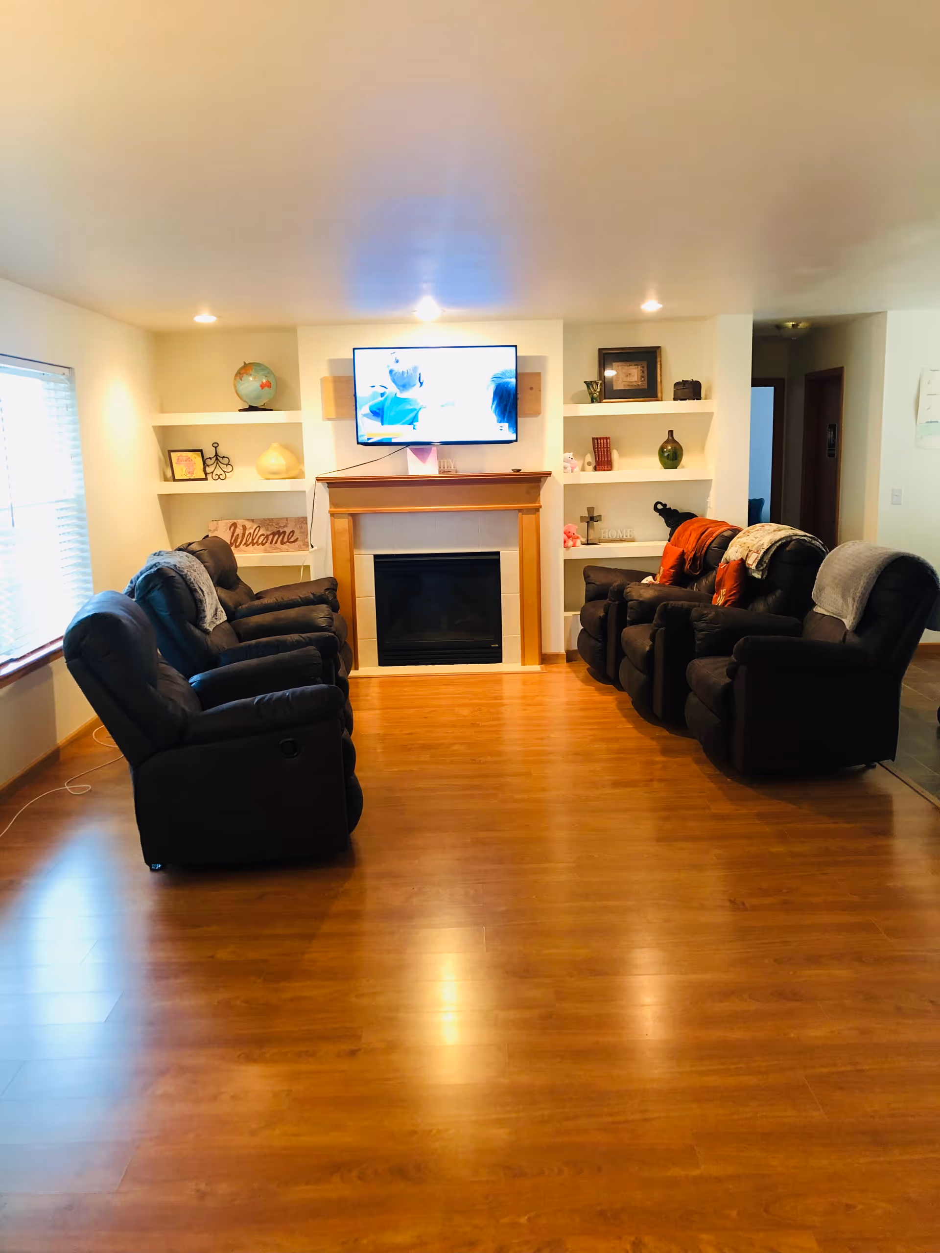 A cozy living room with dark recliners around a fireplace and TV.
