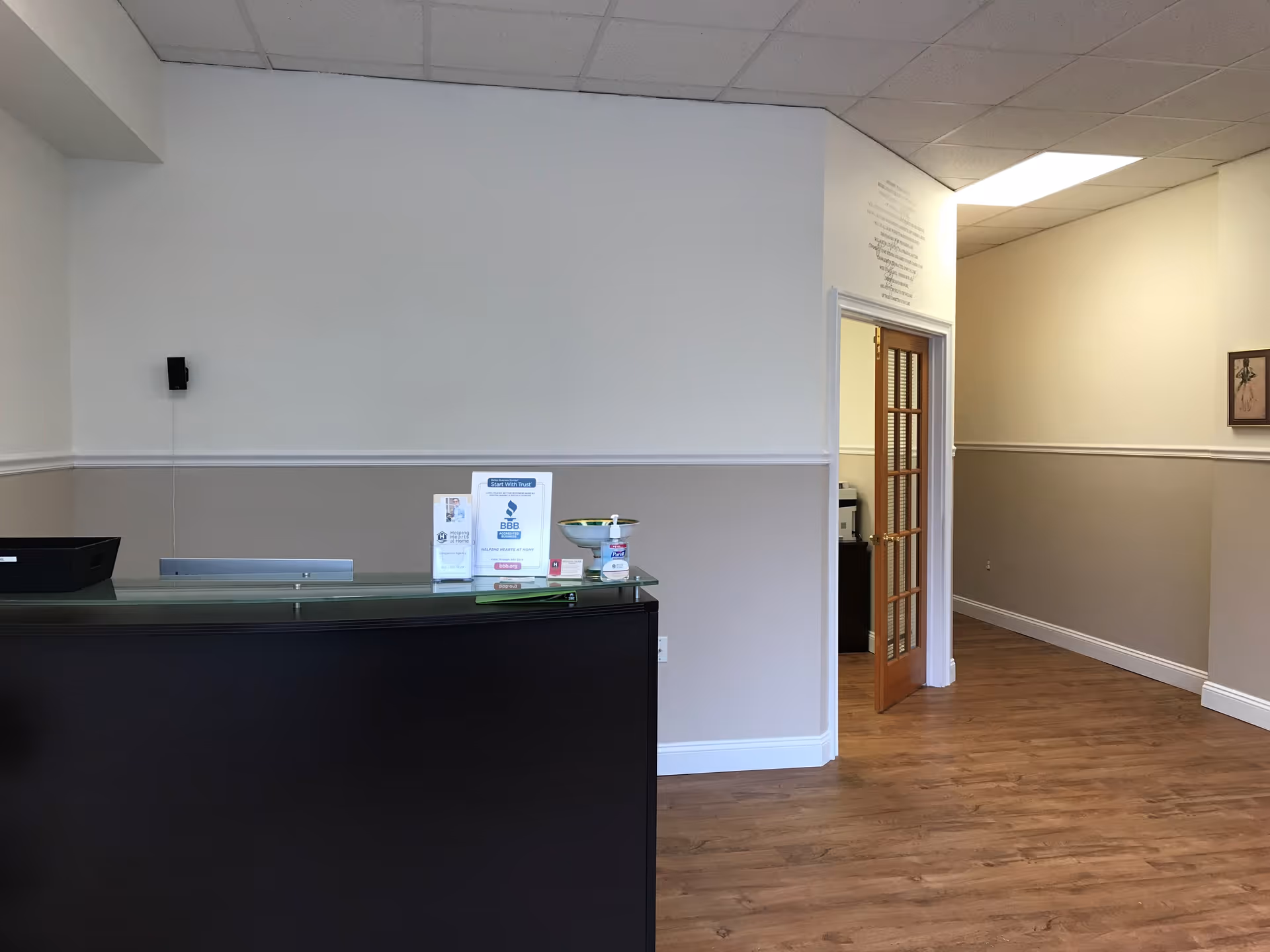 Reception desk in a spacious, neutral lobby with wood flooring and doorway.