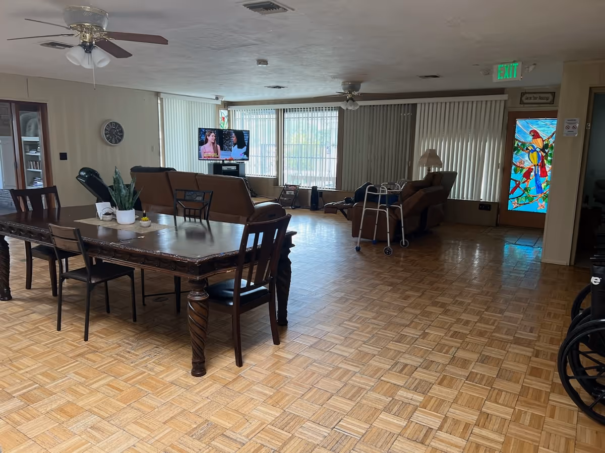 Spacious indoor common area with a large wooden dining table, sofas, TV, and windows.