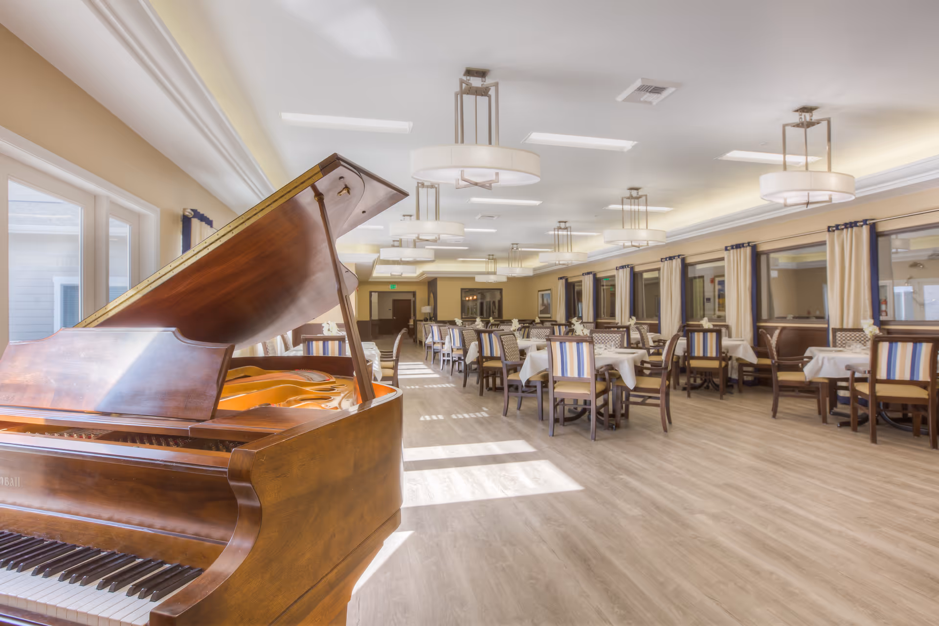 A spacious dining hall with a grand piano and multiple tables set for seating.