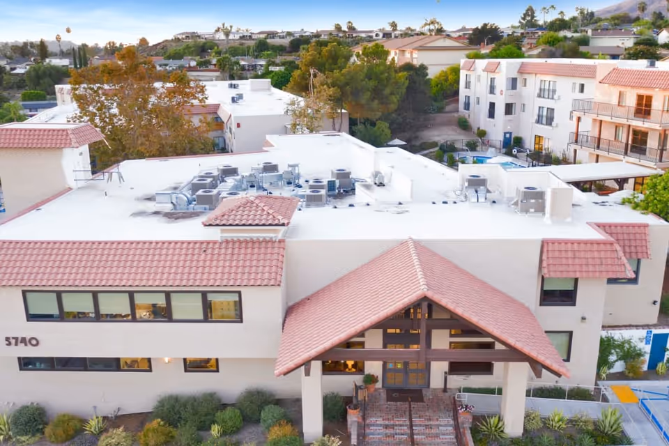 Front exterior of a multi-story senior living building with a tiled entrance canopy, windows, and rooftop HVAC units.
