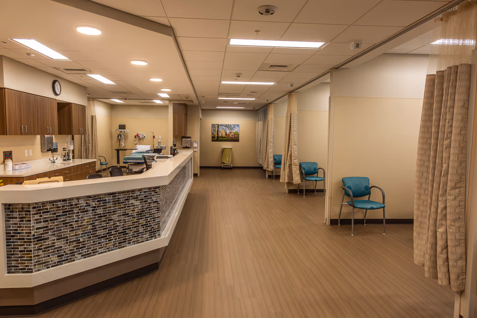 Long reception desk with tiled front, medical equipment, curtains, and seating along an interior hallway.