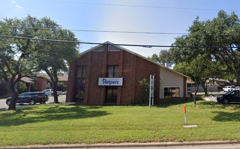 Front view of a Senior Helpers facility with brick exterior, sign, trees, and a grassy lawn.