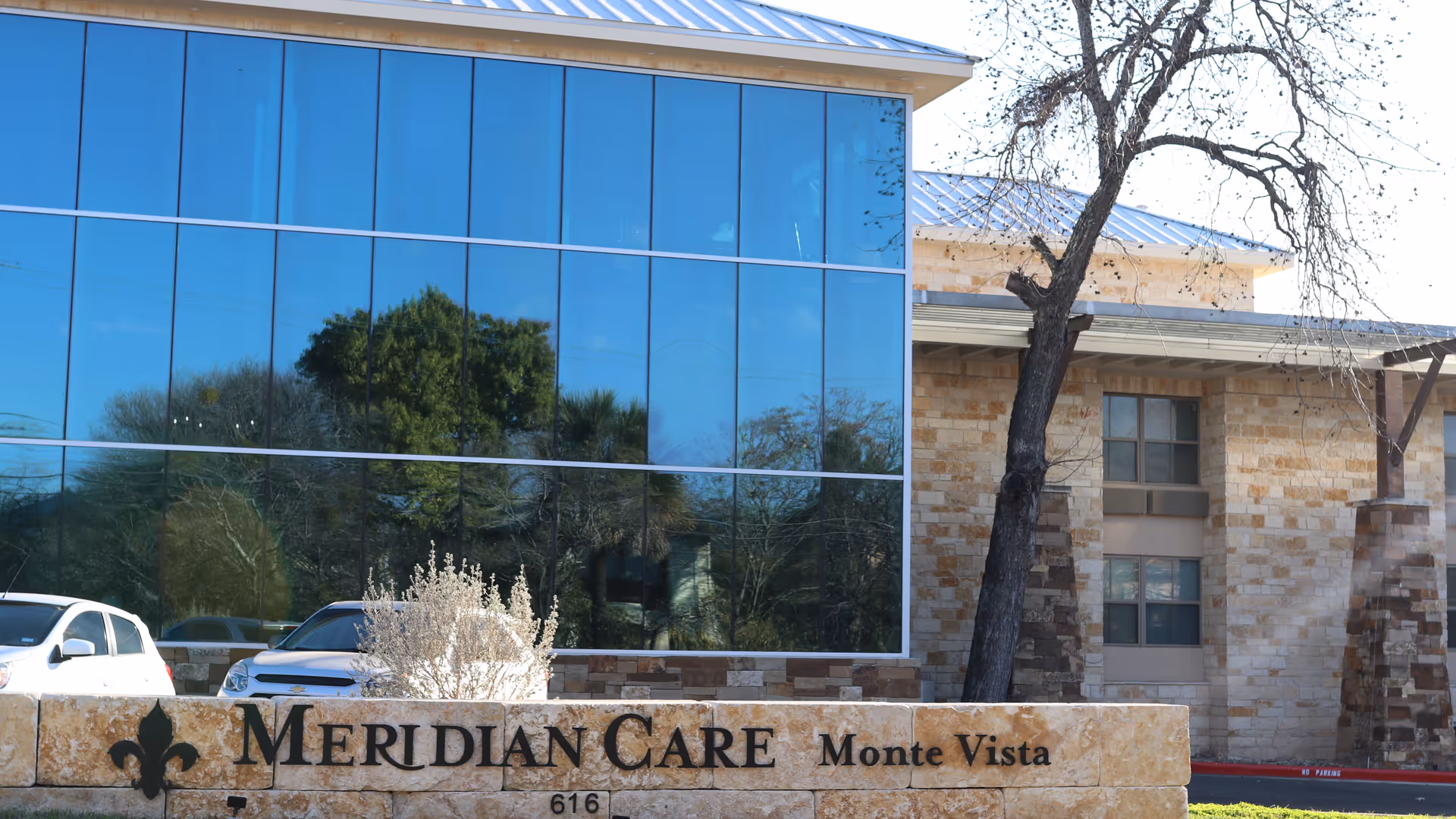 Exterior view of Meridian Care Monte Vista facility with stone sign and glass facade.