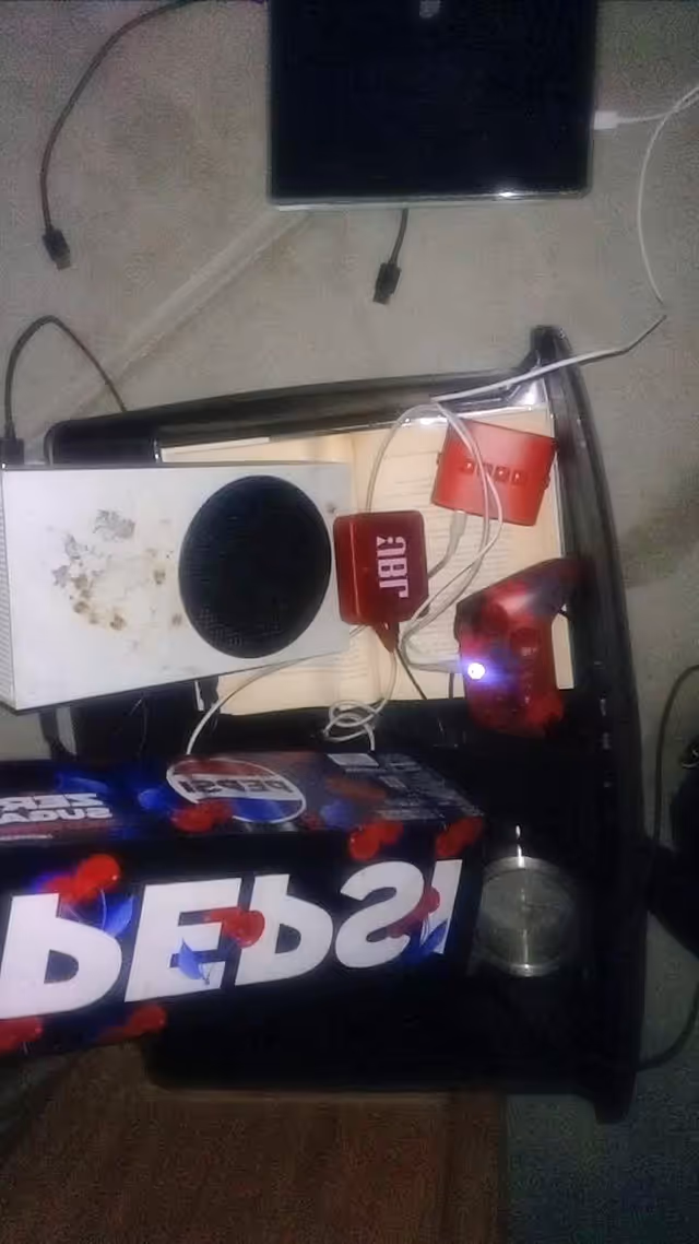 Cluttered desk with electronic devices, cables, and a speaker.