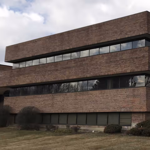 Brick, three-story facility exterior with continuous windows and manicured shrubs in front.