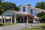 White senior living center with covered entrance, arched windows, and manicured landscaping.