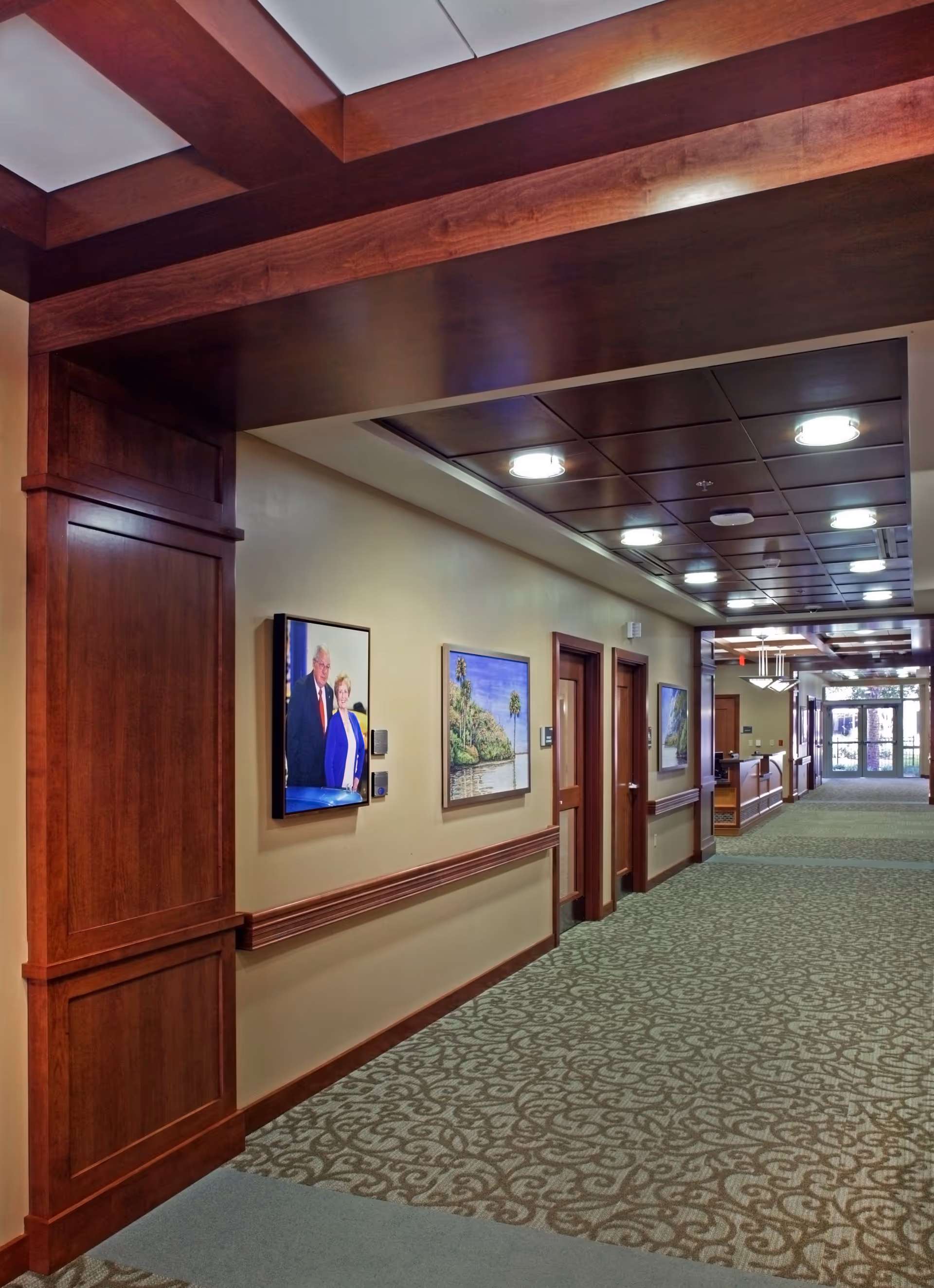 Wood-paneled hallway in a senior living facility with framed wall art.