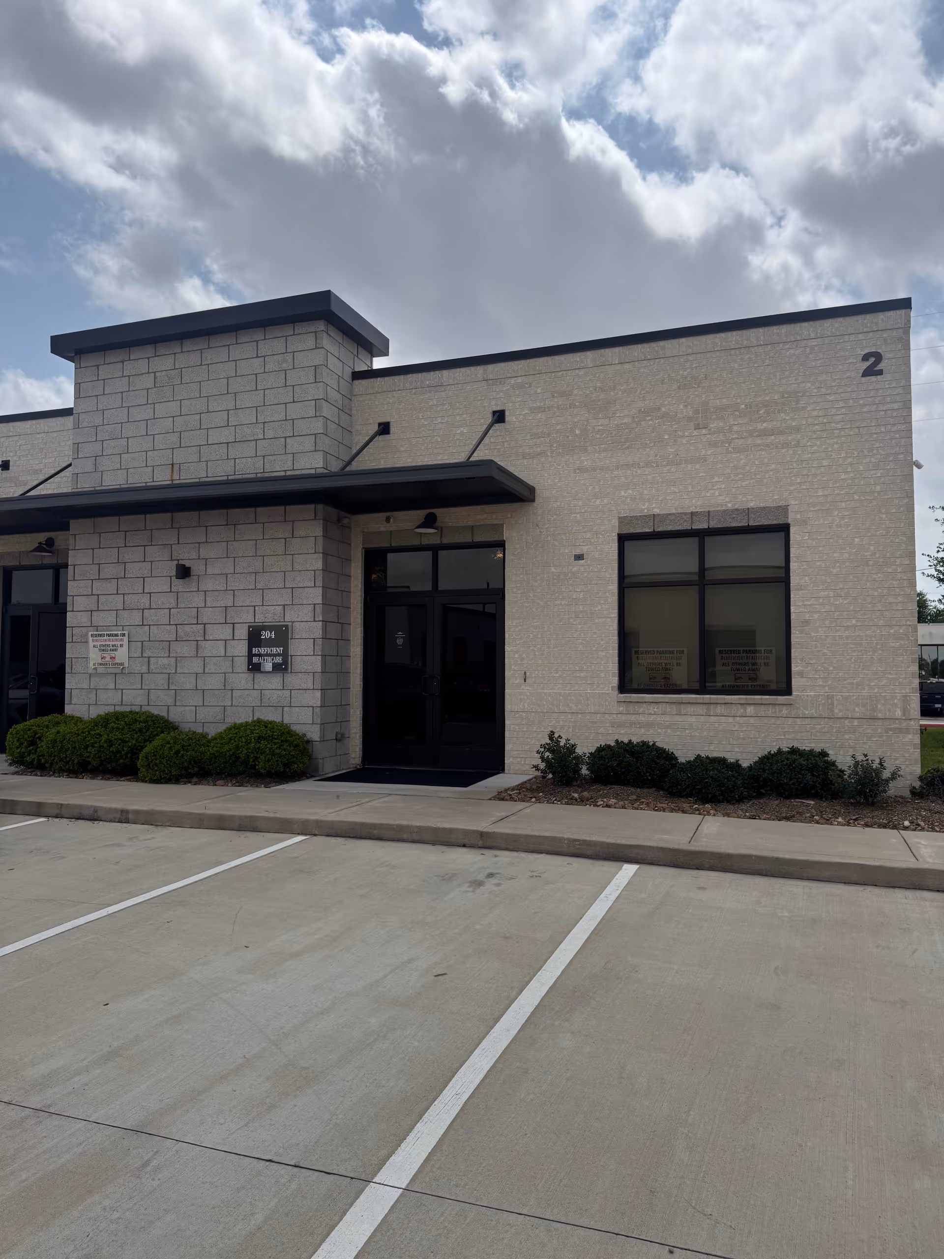 Exterior view of a beige brick senior living facility entrance with parking lot.