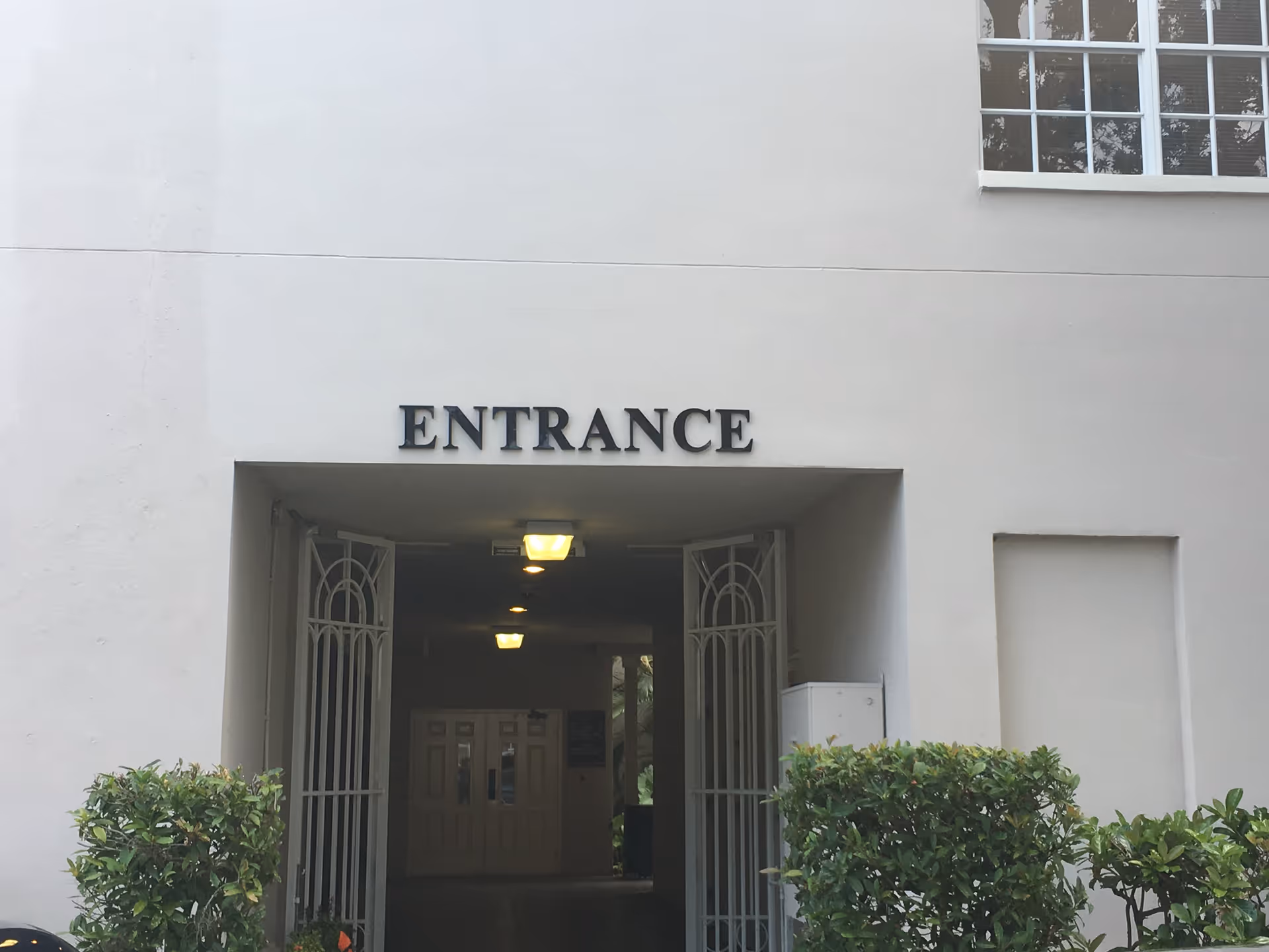 White building entrance labeled ENTRANCE with open metal gates and a lit interior hallway.