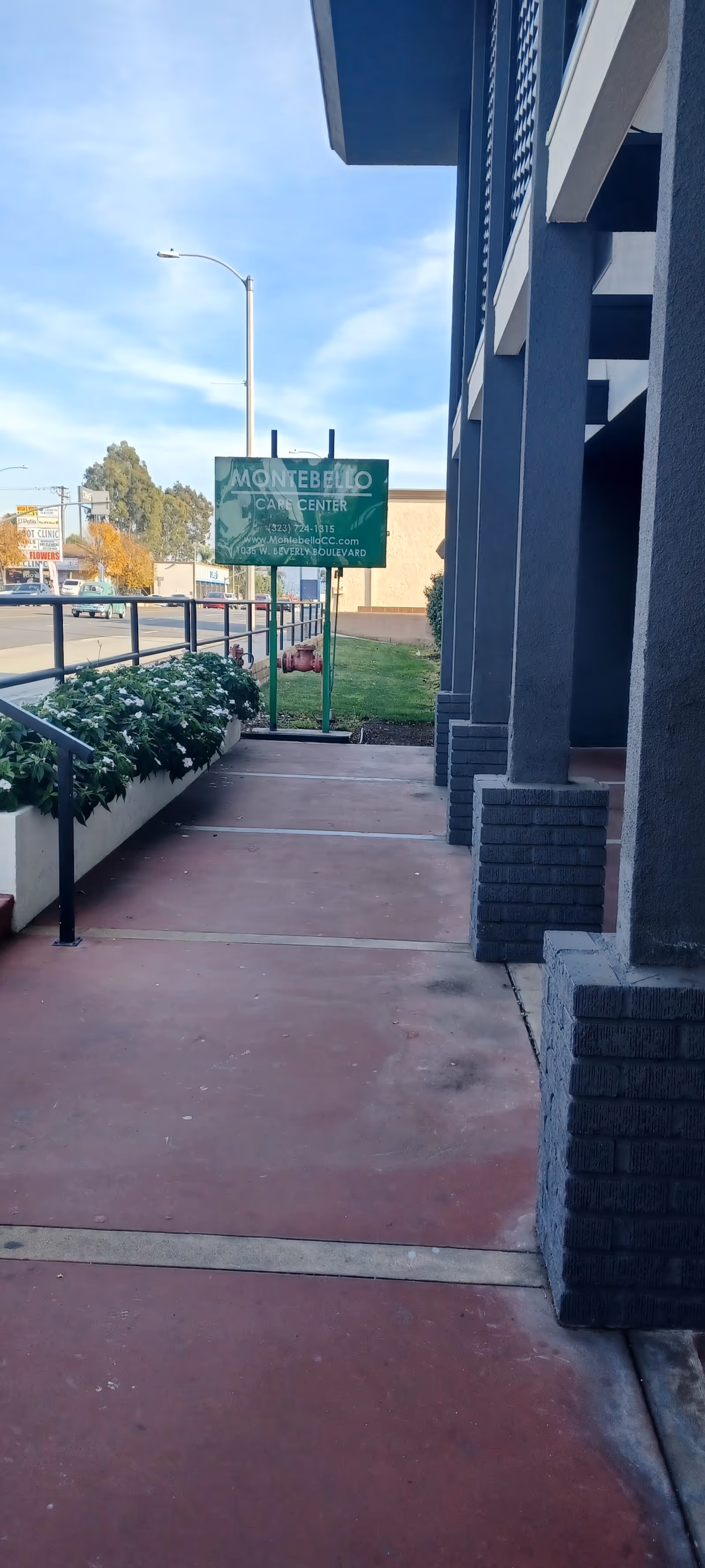 Outdoor walkway beside Montebello Care Center with planters, railing, and building columns.