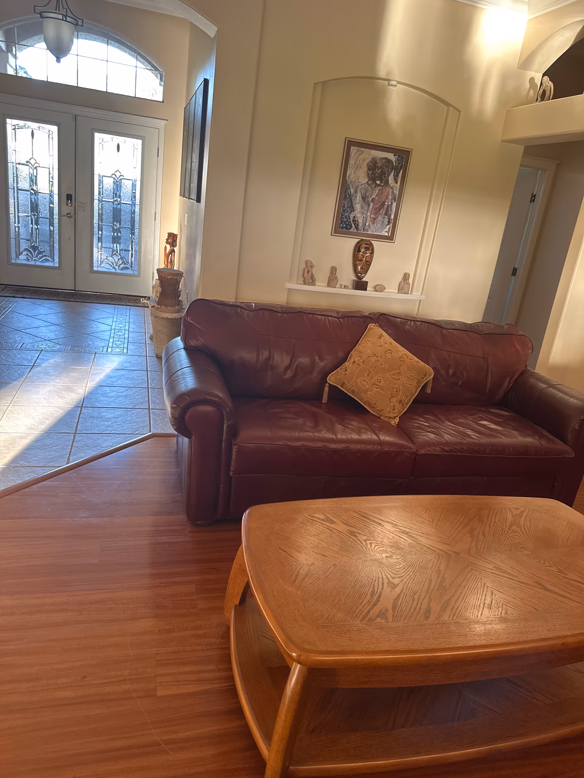 Cozy living room with burgundy leather sofa, wooden coffee table, and glass entry doors.