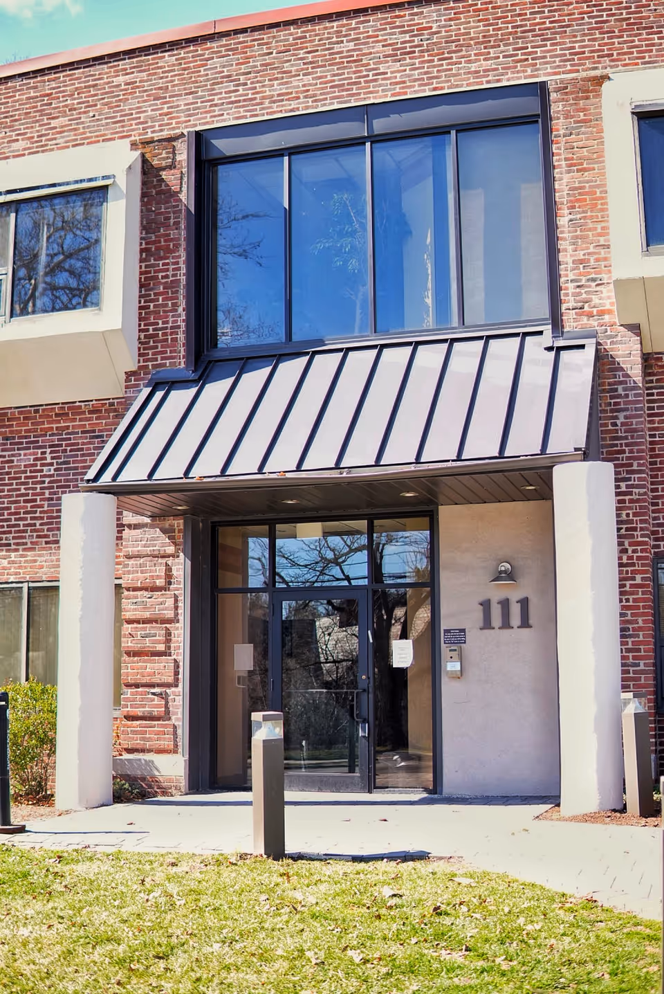 Katura Health brick building entrance with glass doors, metal awning, and tall windows.
