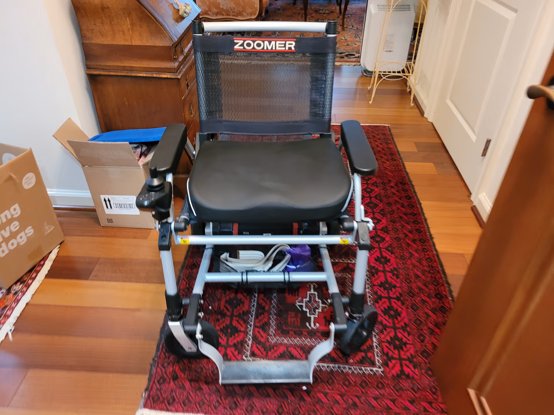 A Zoomer wheelchair sits in a narrow hallway on a red rug.