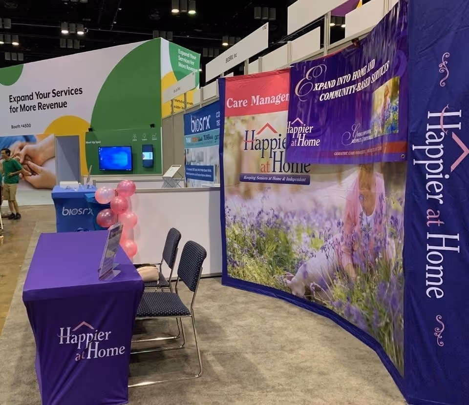 Trade show booth with Happier at Home banners in a purple themed expo hall.