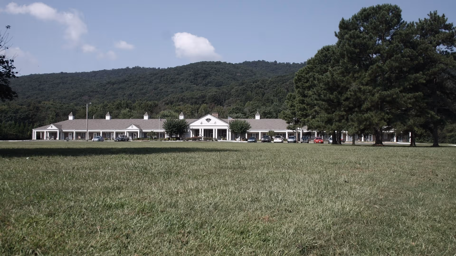 View of Oaks at Dalton senior living facility from a grassy field with parked cars.