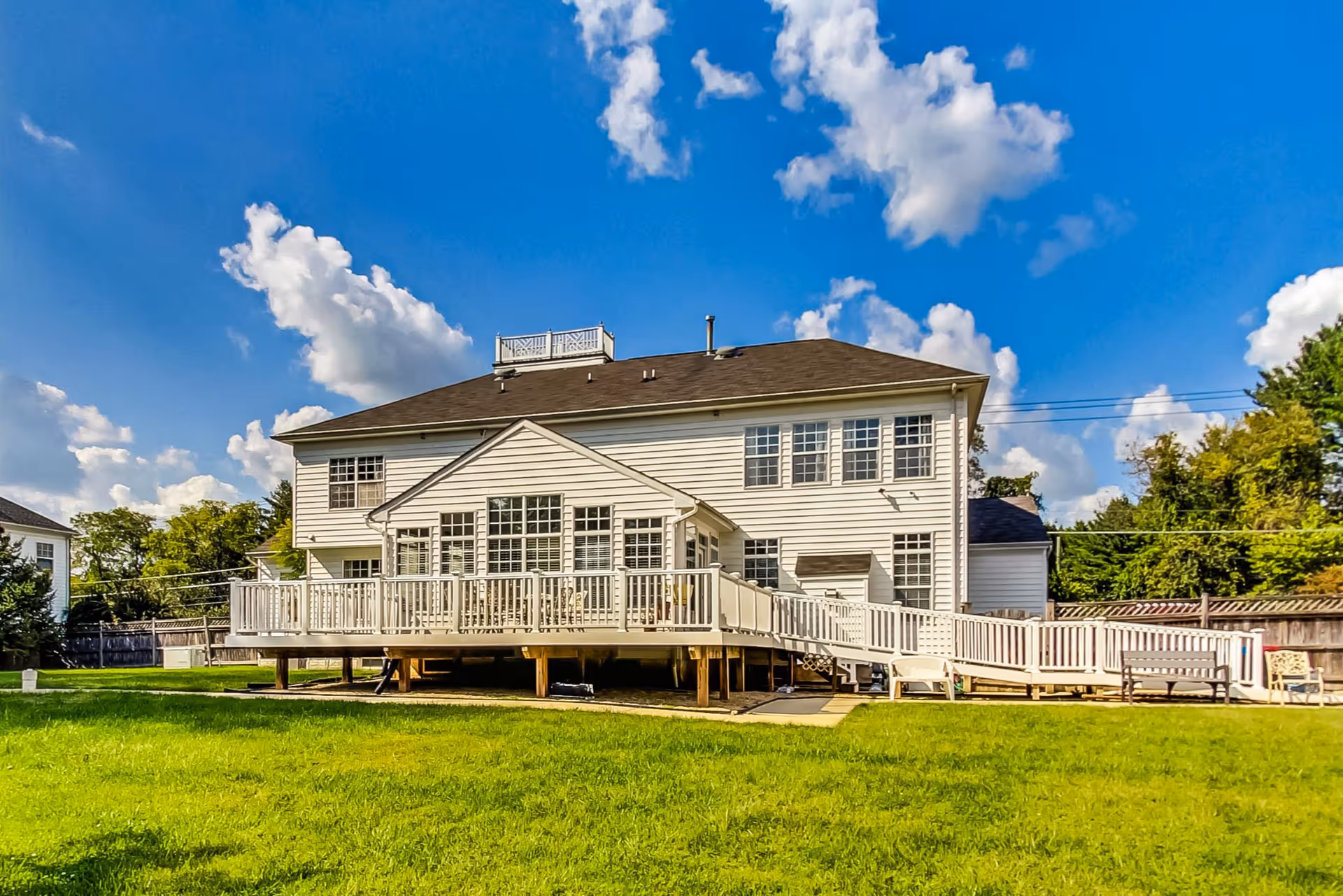White two-story assisted living building with a long deck, green lawn, and blue sky.