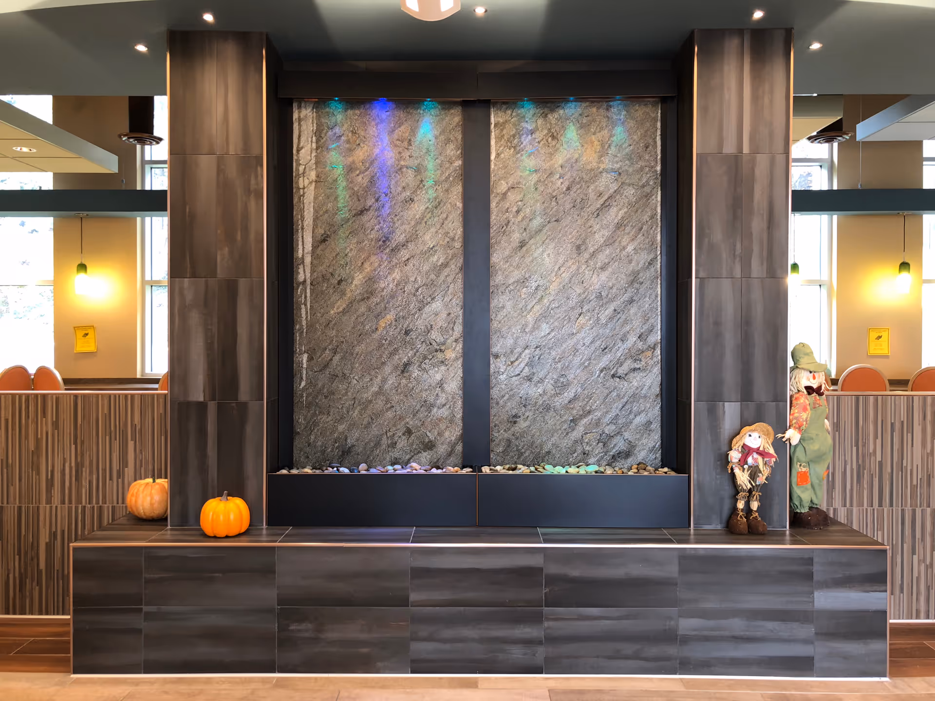 A stone wall fountain centerpiece inside a lobby with pumpkins and scarecrows as decor