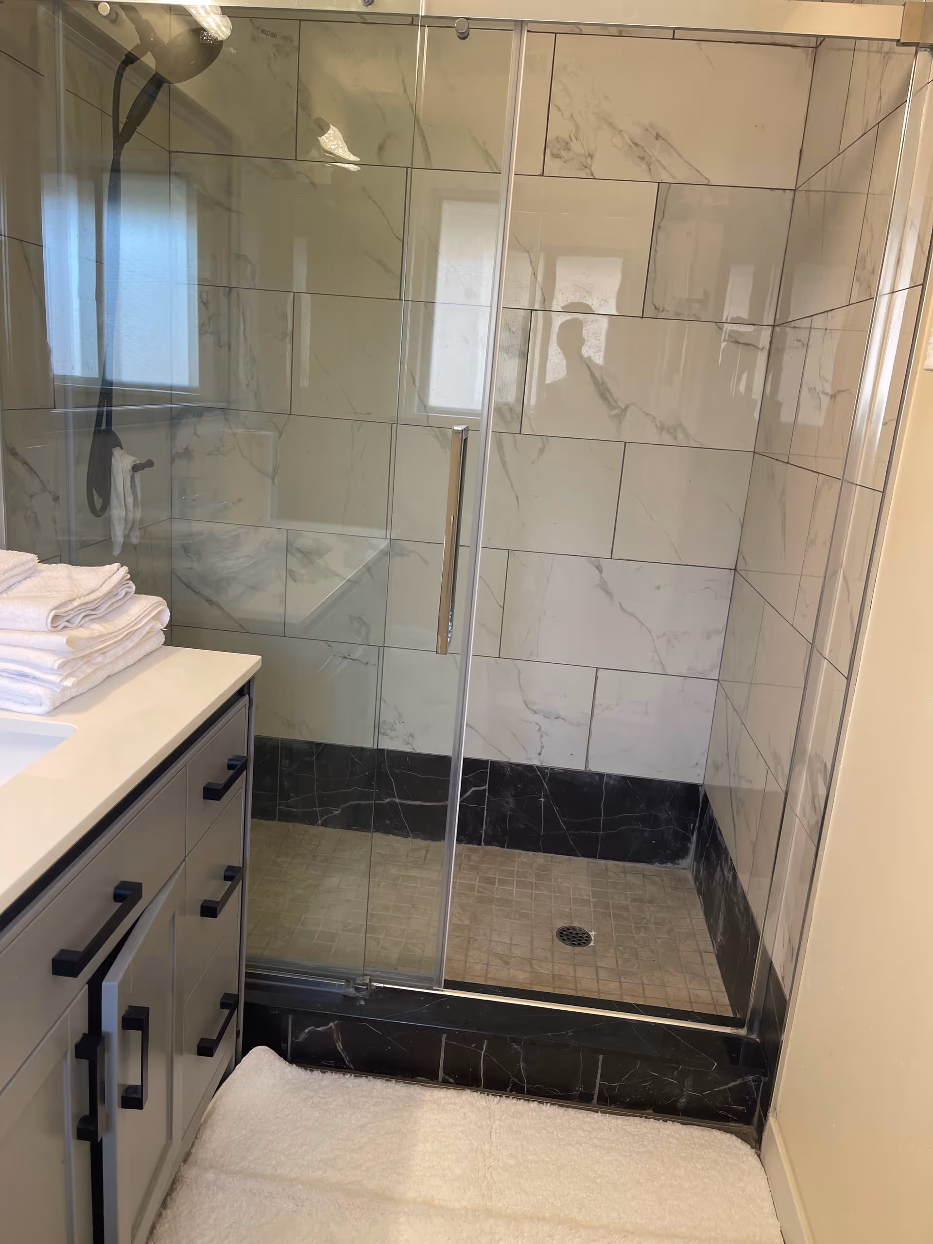 Modern bathroom with glass shower enclosure, marble tile walls, and a vanity with towels.