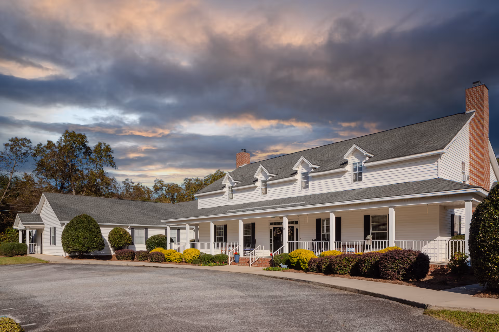 Exterior view of The Oaks Peake facility with white siding, shrubs, and a parking area.