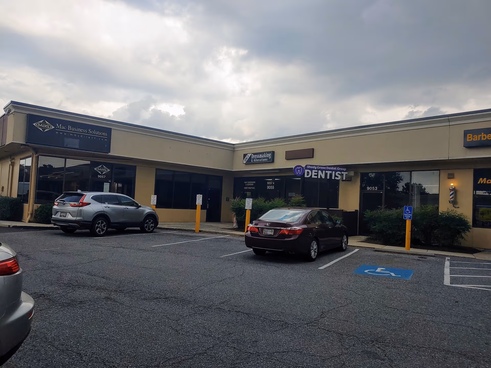 Exterior view of a single-story strip mall with parked cars and business signs.