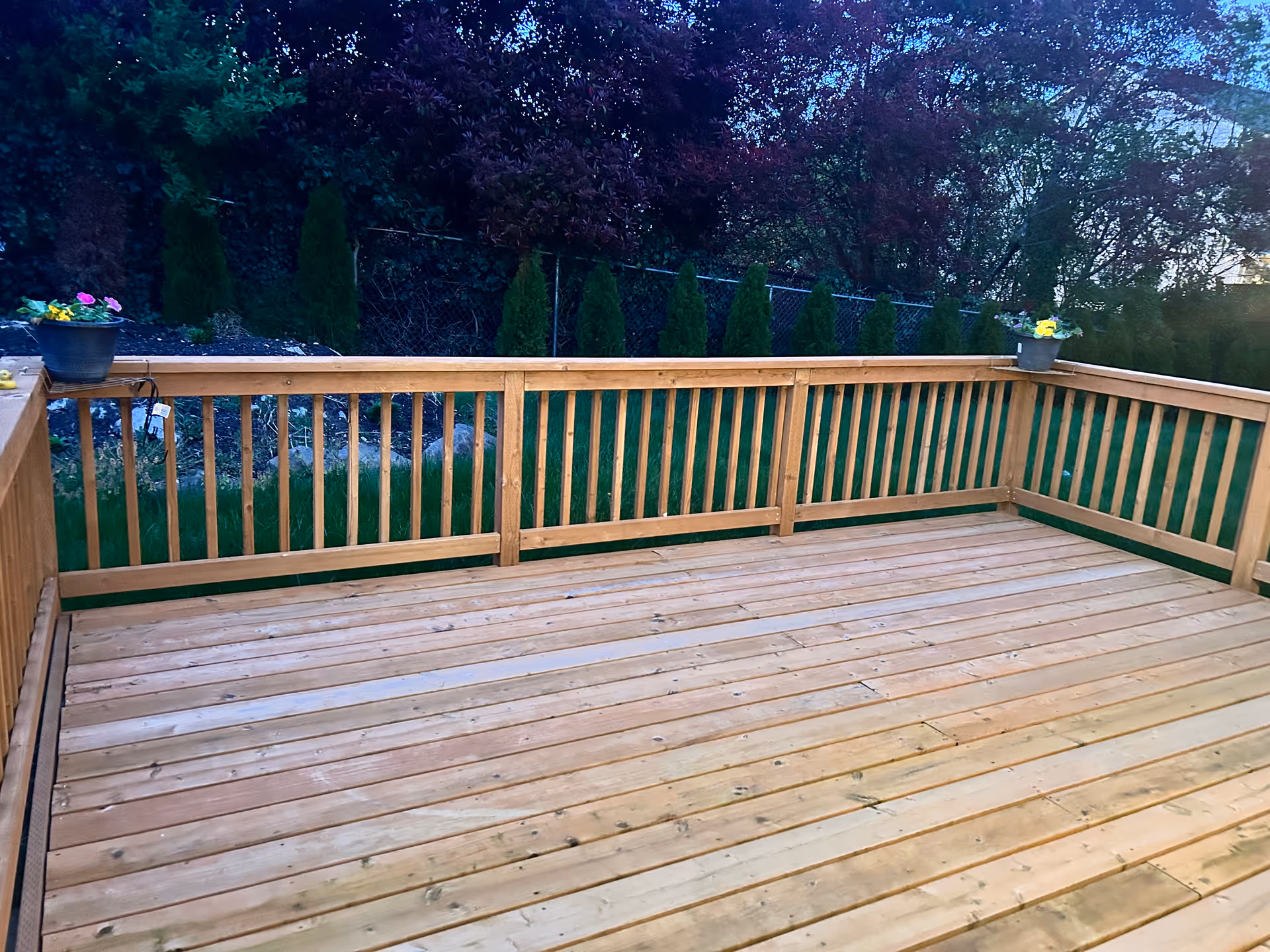 Empty wooden deck with railing and potted flowers overlooking a green backyard.