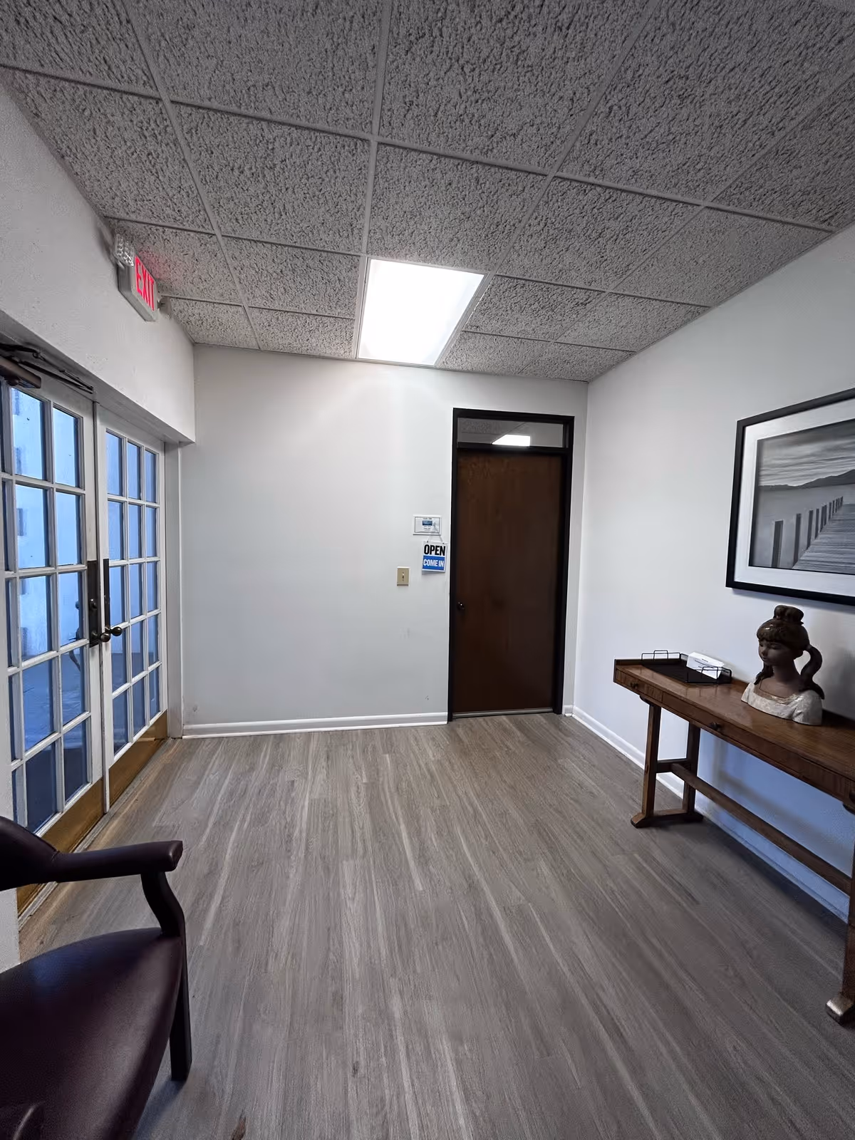 Interior hallway with glass doors, seating, a wooden console table, and a statue bust.