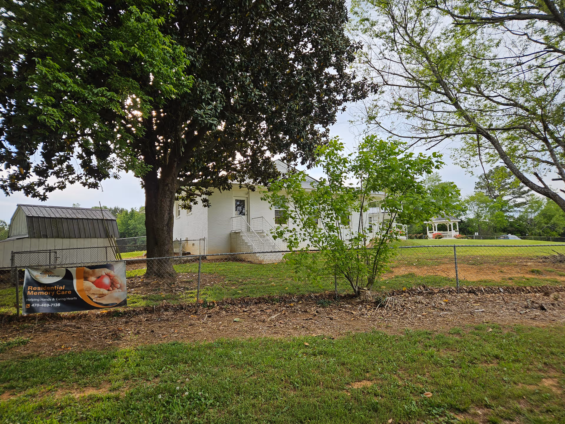 Exterior view of Ridge Manor of Calhoun with a fence, trees, and a memory care banner.