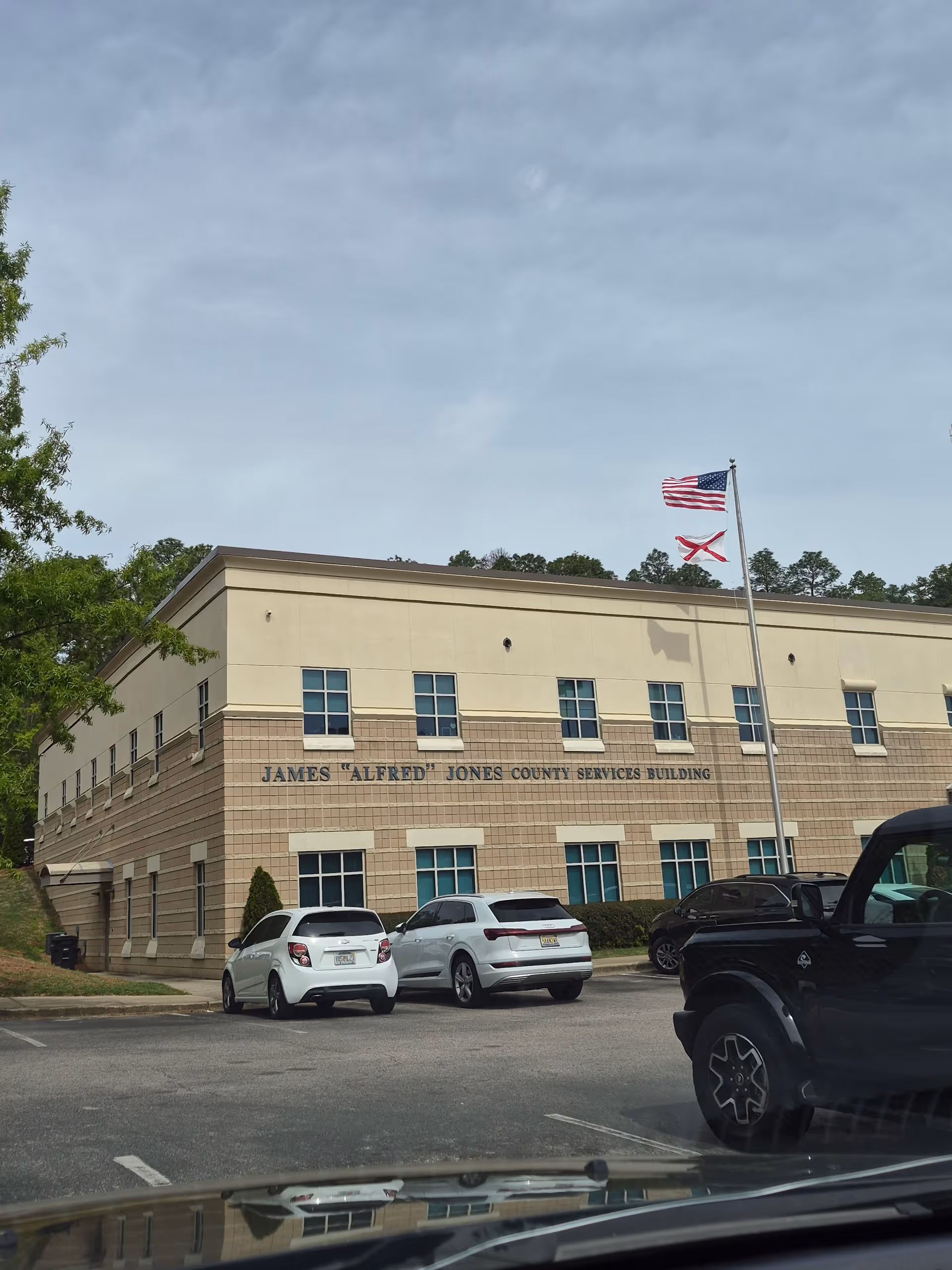 Exterior view of a beige, two-story building with flags and parked cars.