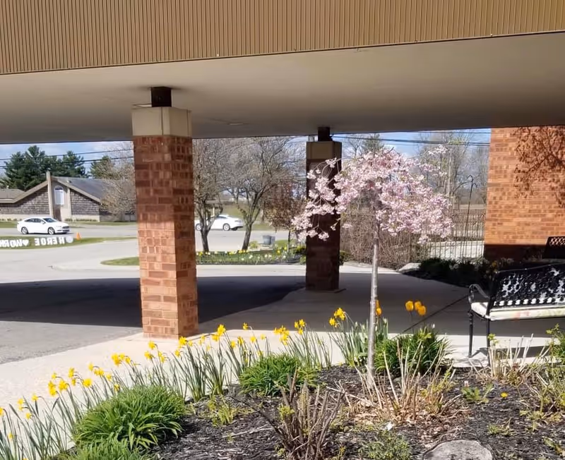 Covered outdoor entrance at Alice Lorraine Care Center with brick columns and flowers.