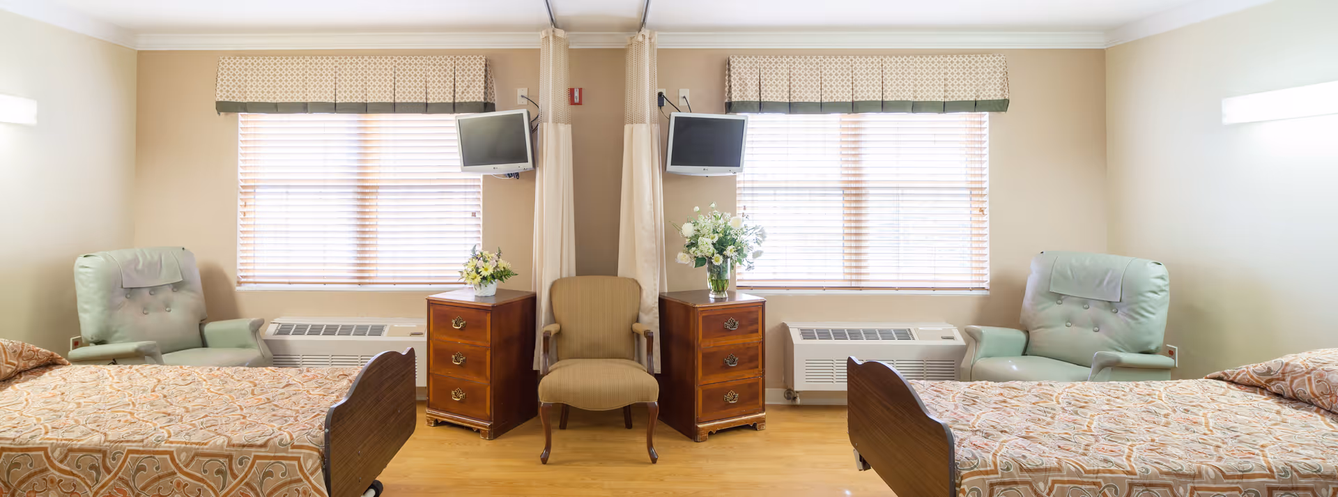 Symmetrical shared bedroom with two beds, armchairs, nightstands, and windows with blinds.