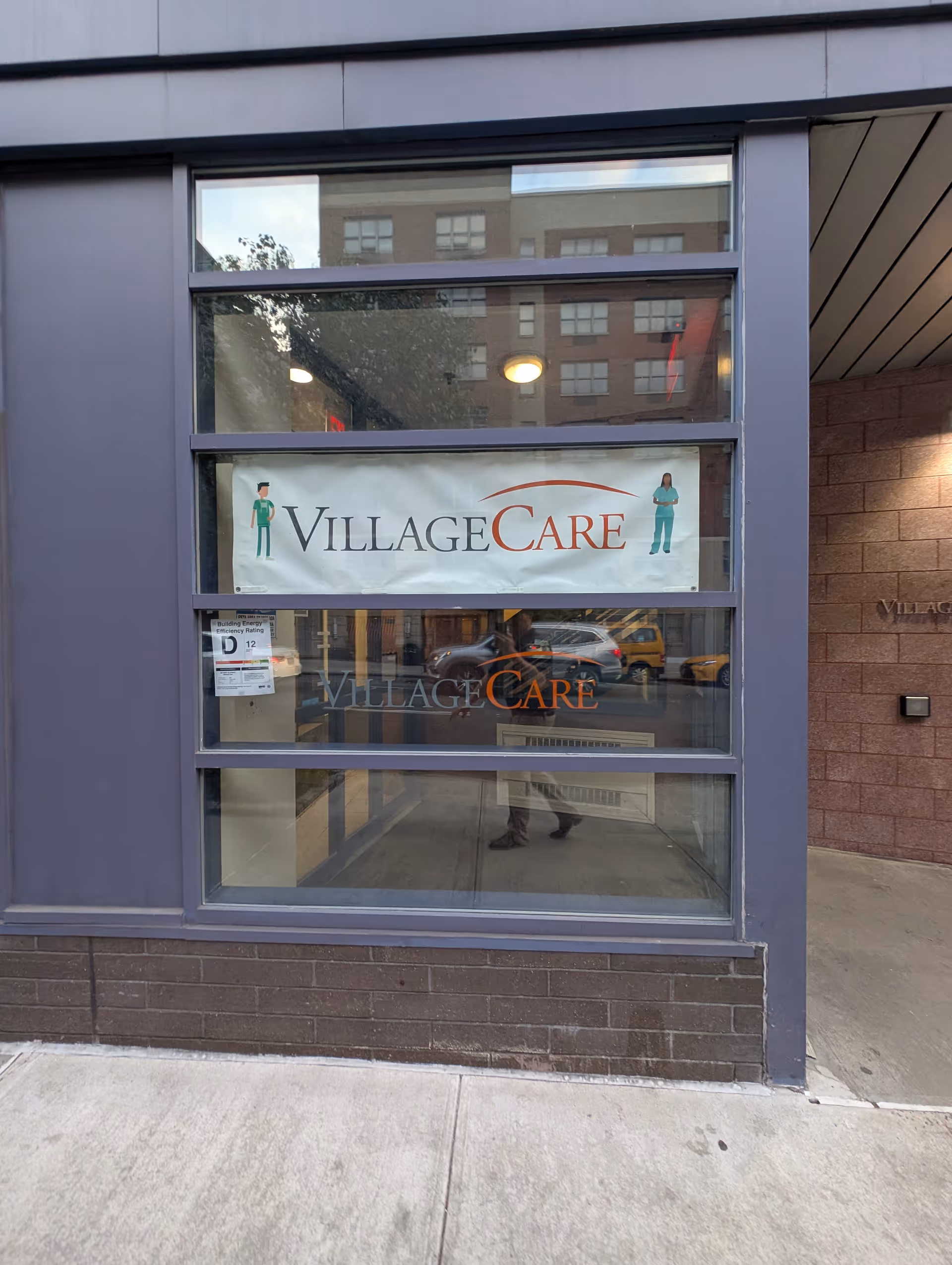 Front view of VillageCare storefront with a large window banner displaying the VillageCare logo.