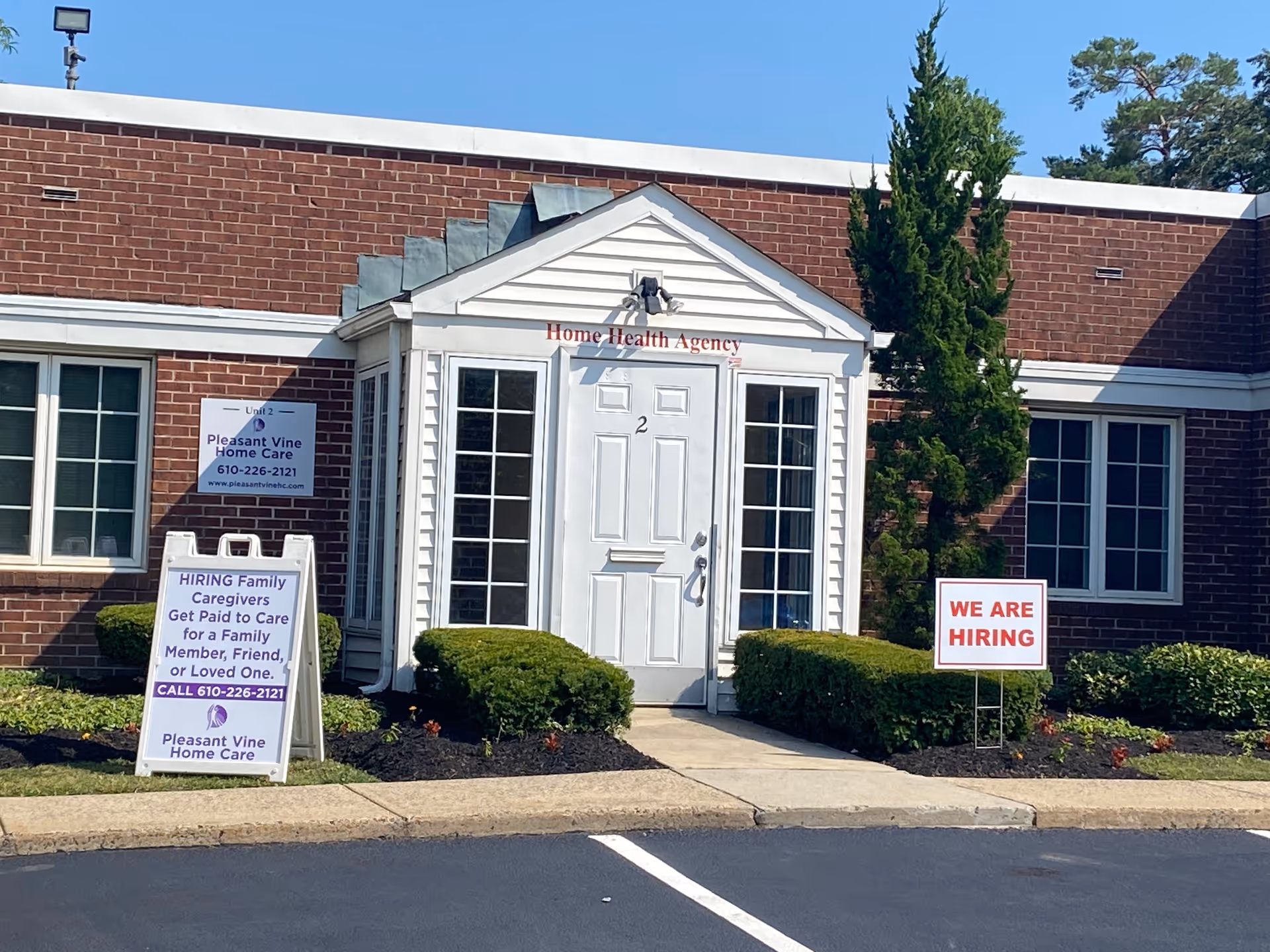 Front view of Pleasant Vine Home Care building with hiring signs and shrubs.