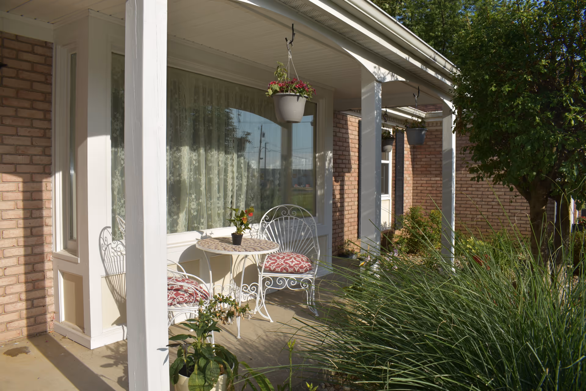 Porch of a senior living facility with white wrought-iron chairs and hanging planters