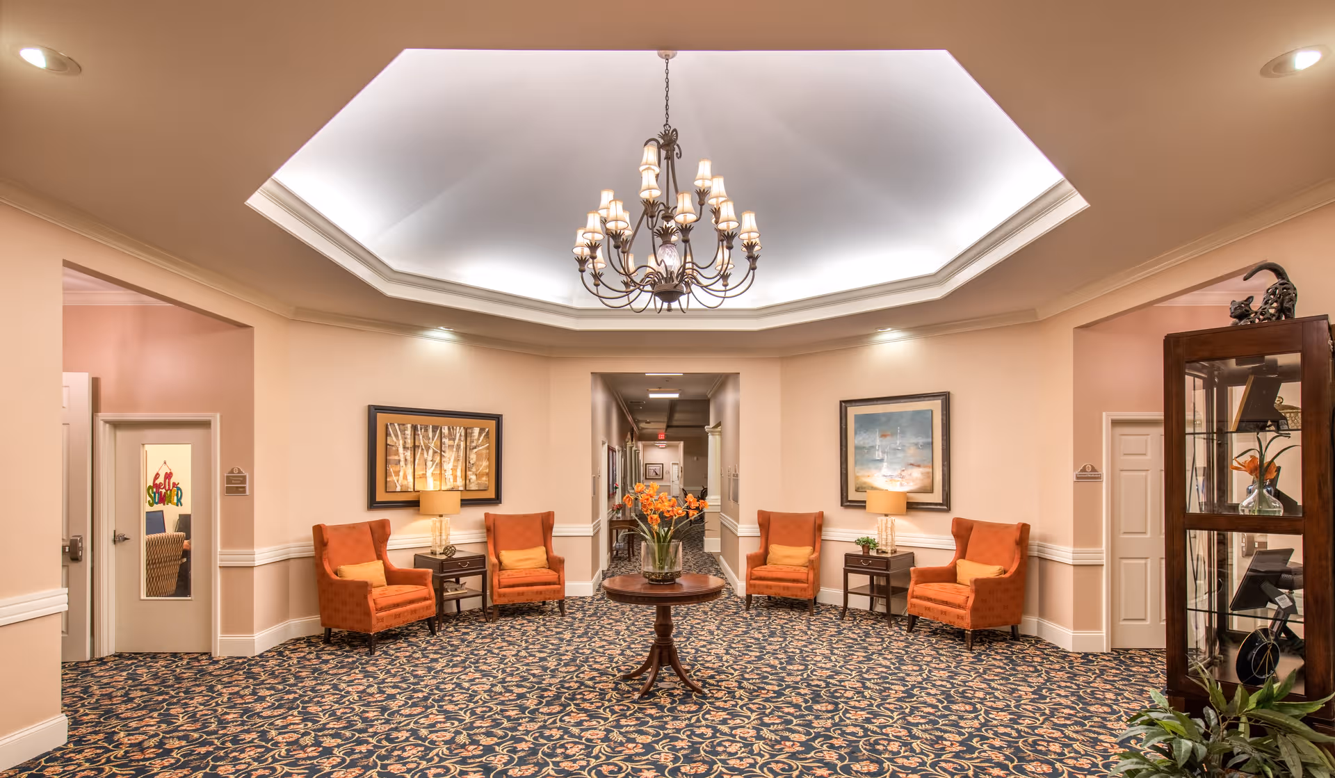 Benton House of Blue Springs lobby with orange chairs around a central table under a chandelier.