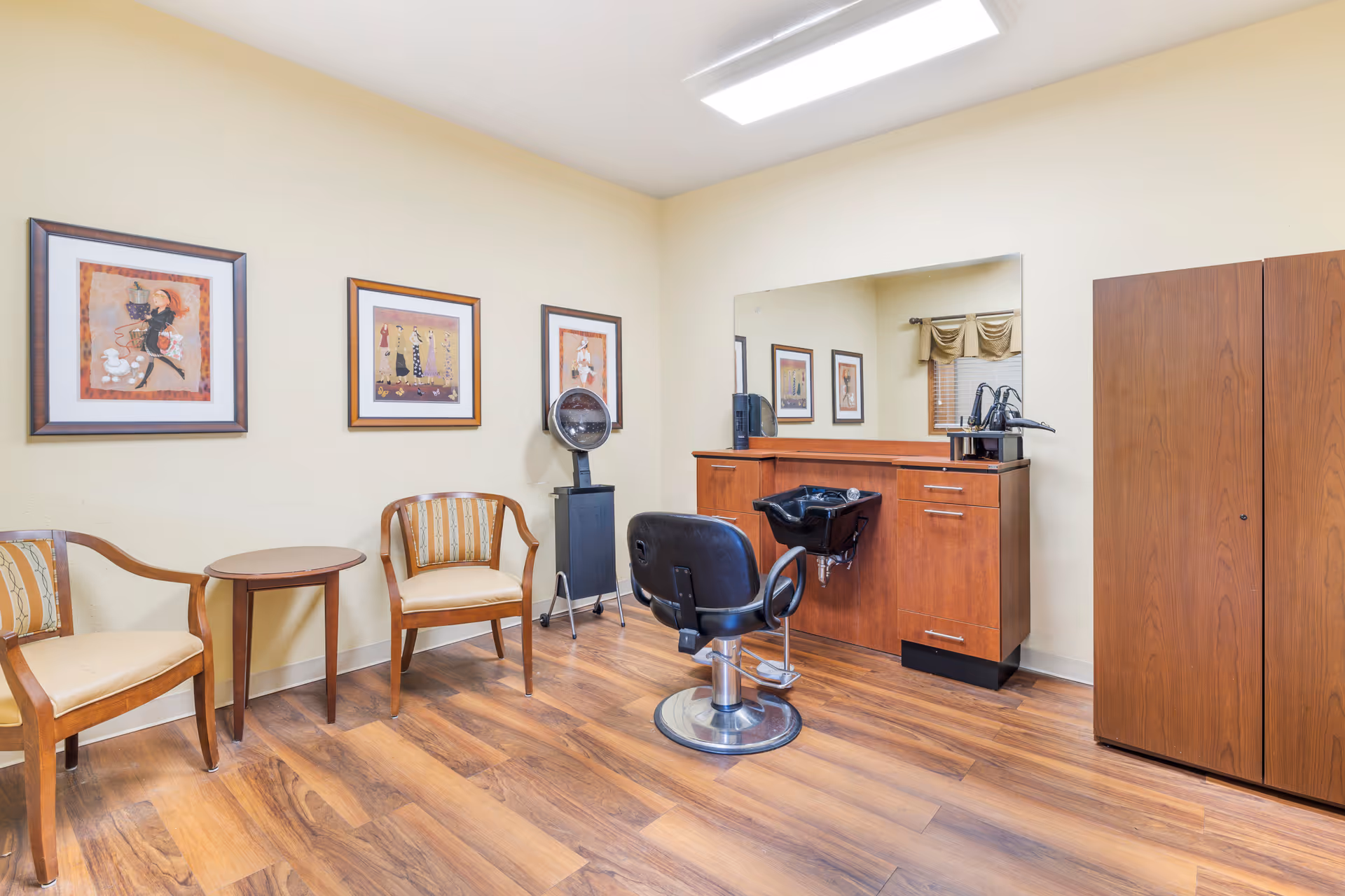 Hair salon inside a senior living facility with chairs, cabinets, and a large mirror.