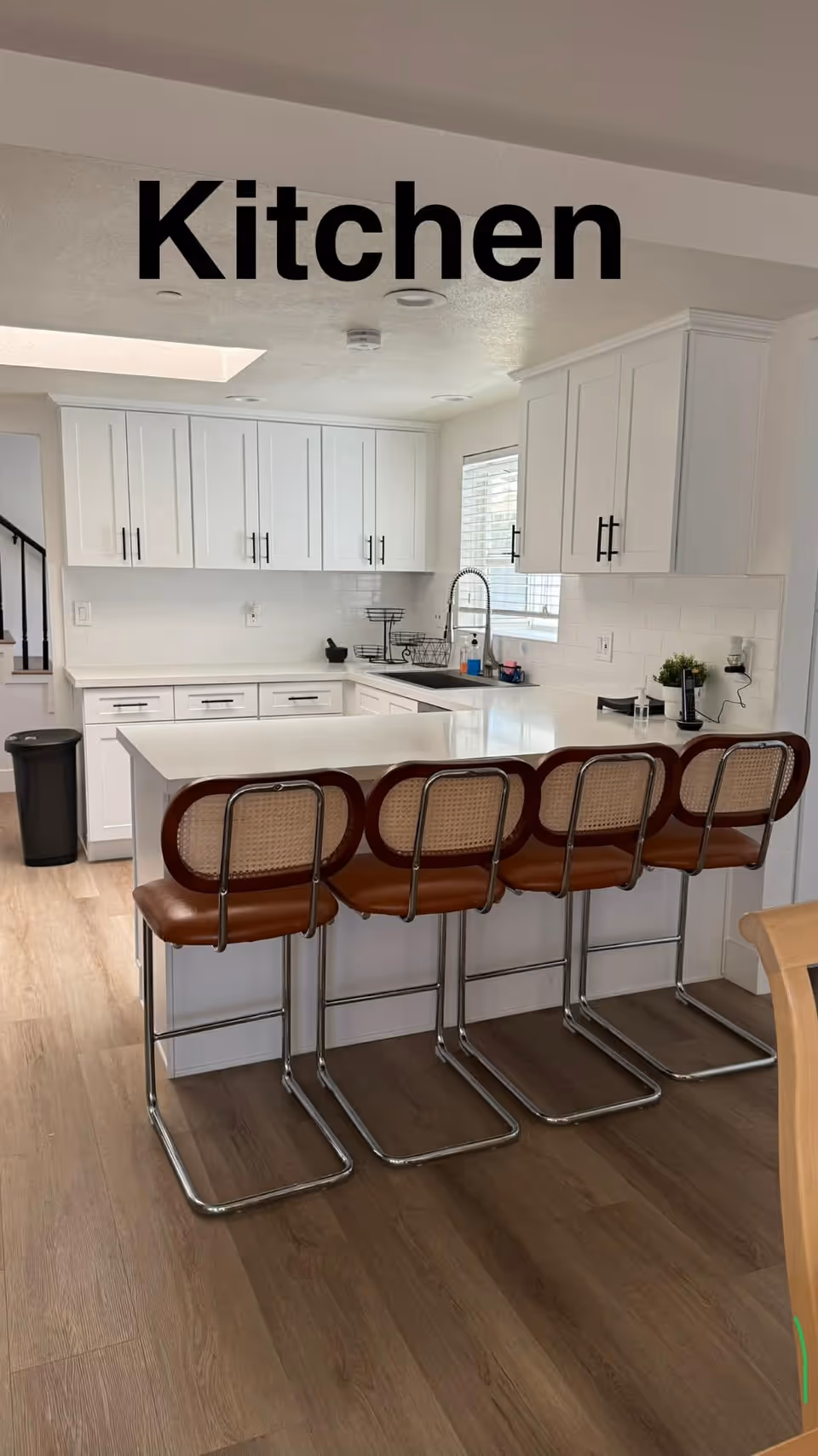 White kitchen with island, cabinets, bar stools, and a stainless sink area.