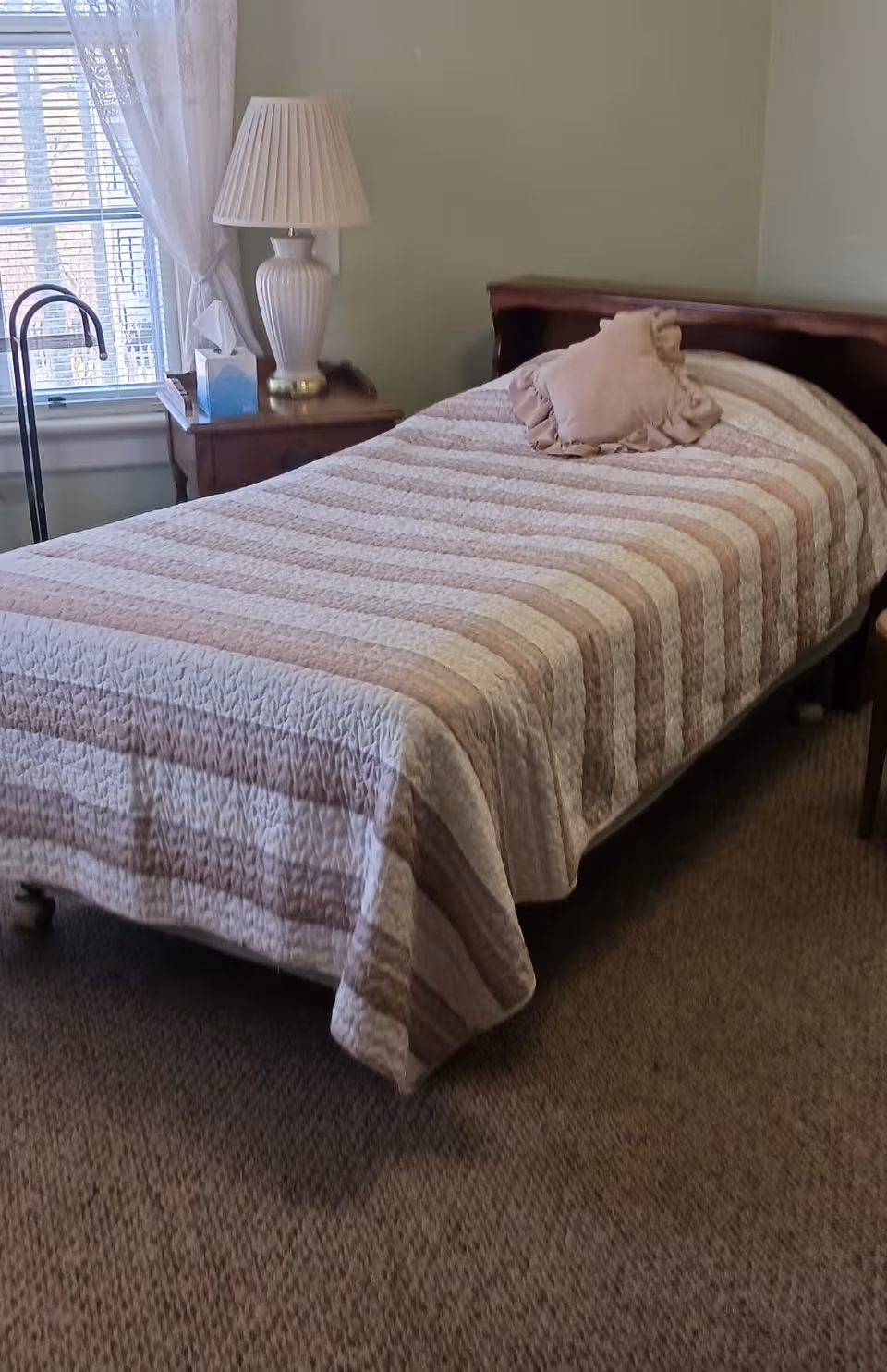 A neatly made single bed with striped quilt in a bedroom with lamp.