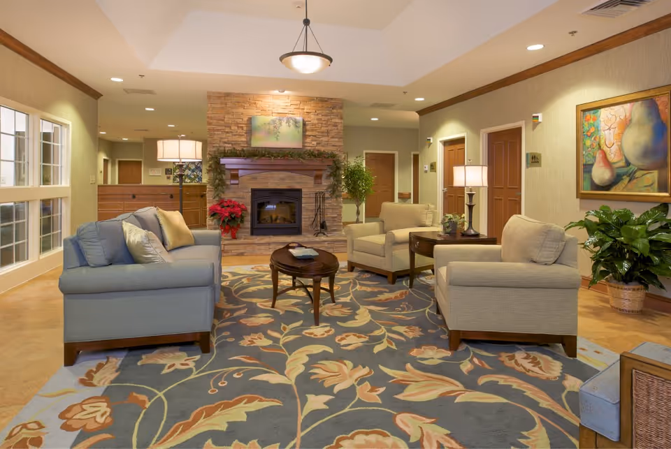 Cozy senior living lobby with sofas, a fireplace, rug, and plants