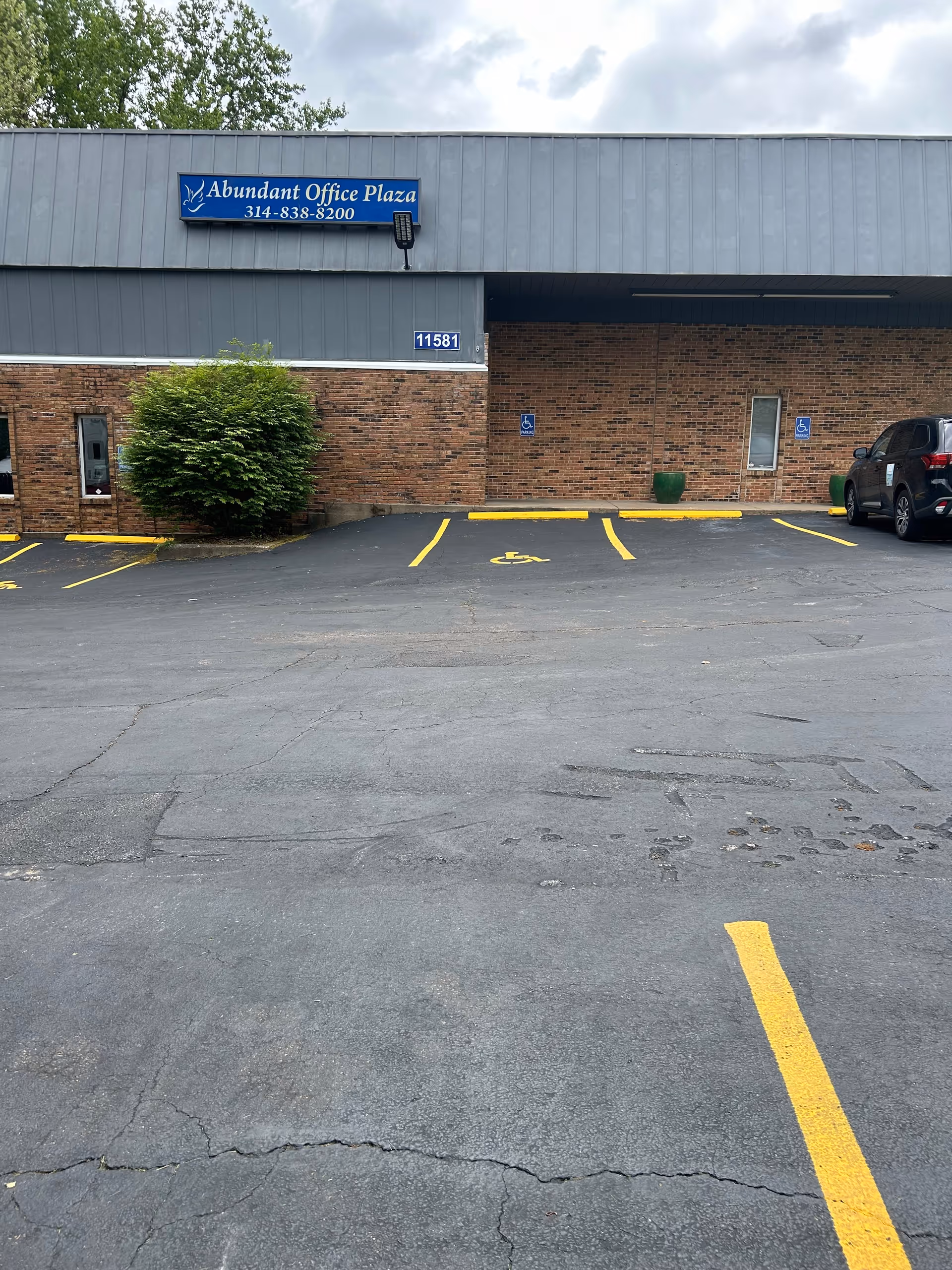 Front of a brick office building with handicap parking and an Abundant Office Plaza sign.