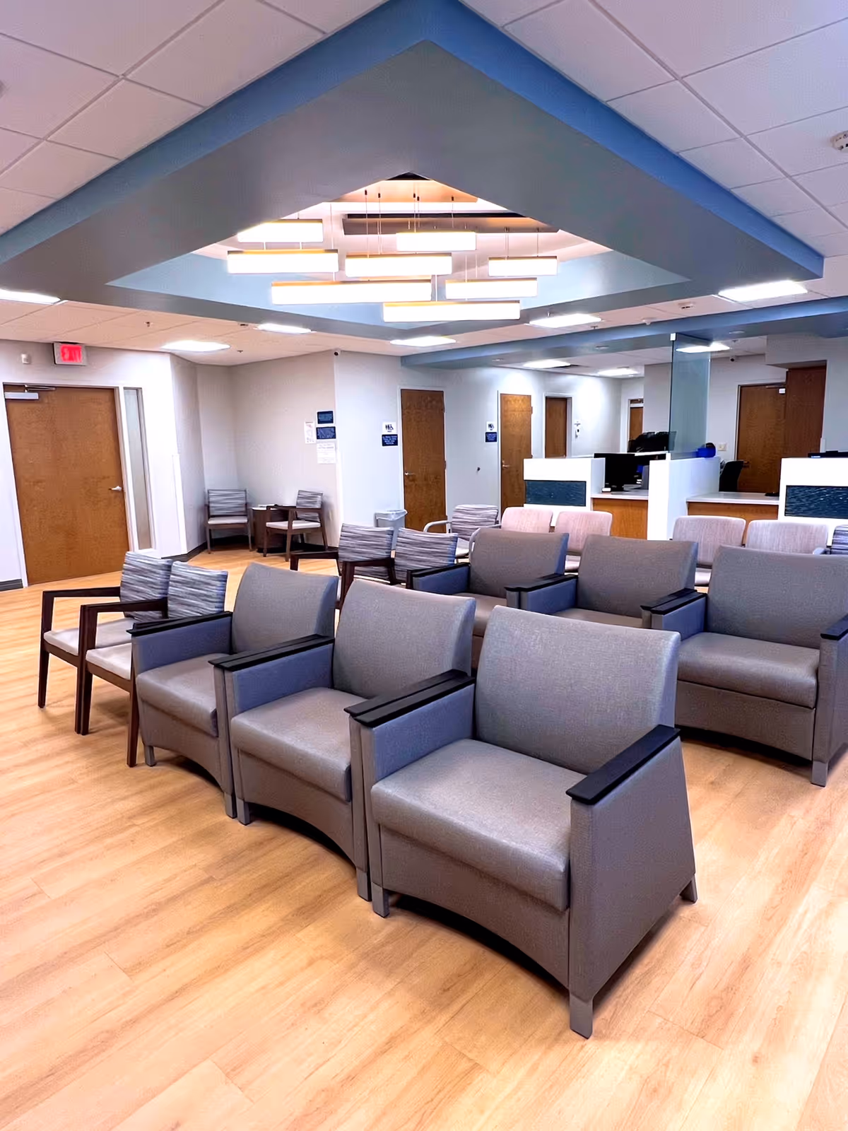 Rows of gray armchairs in a spacious waiting area with a reception desk in the back.
