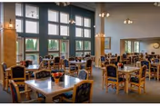 Bright dining room with multiple tables, chairs, and large windows overlooking outdoors.