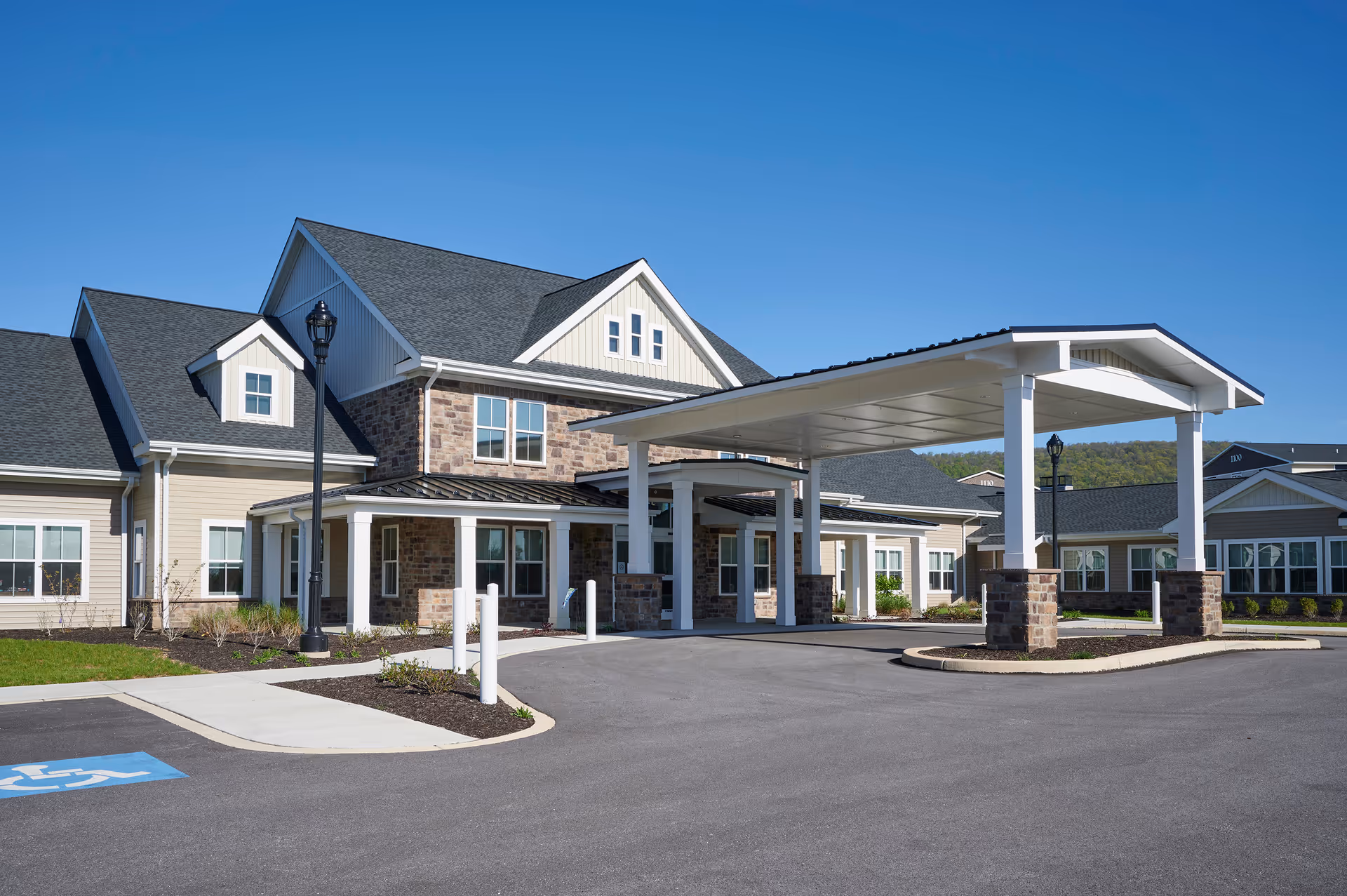 Front entrance of a modern senior living building with a large covered porte-cochere and landscaped driveway.
