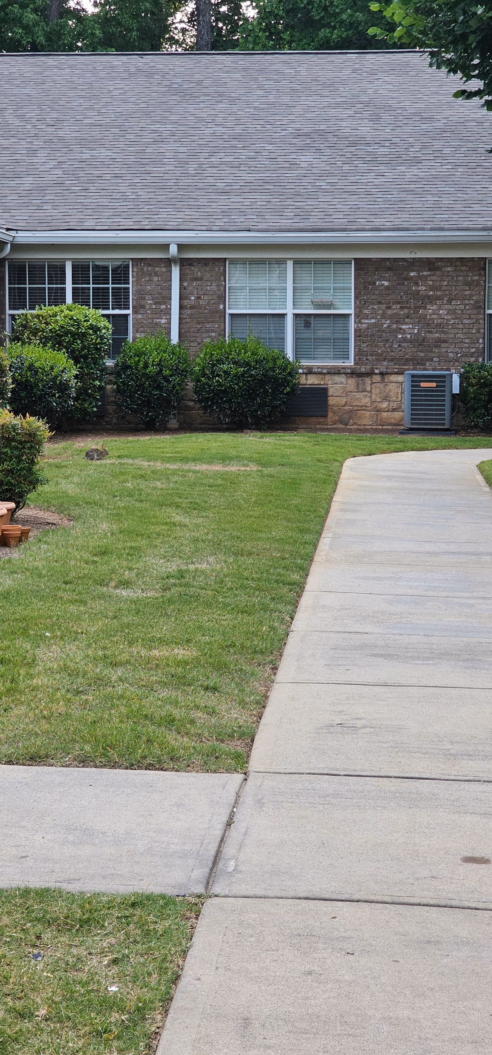 Exterior view of Addington Place of Johns Creek, brick building, sidewalk, greenery, and AC unit.
