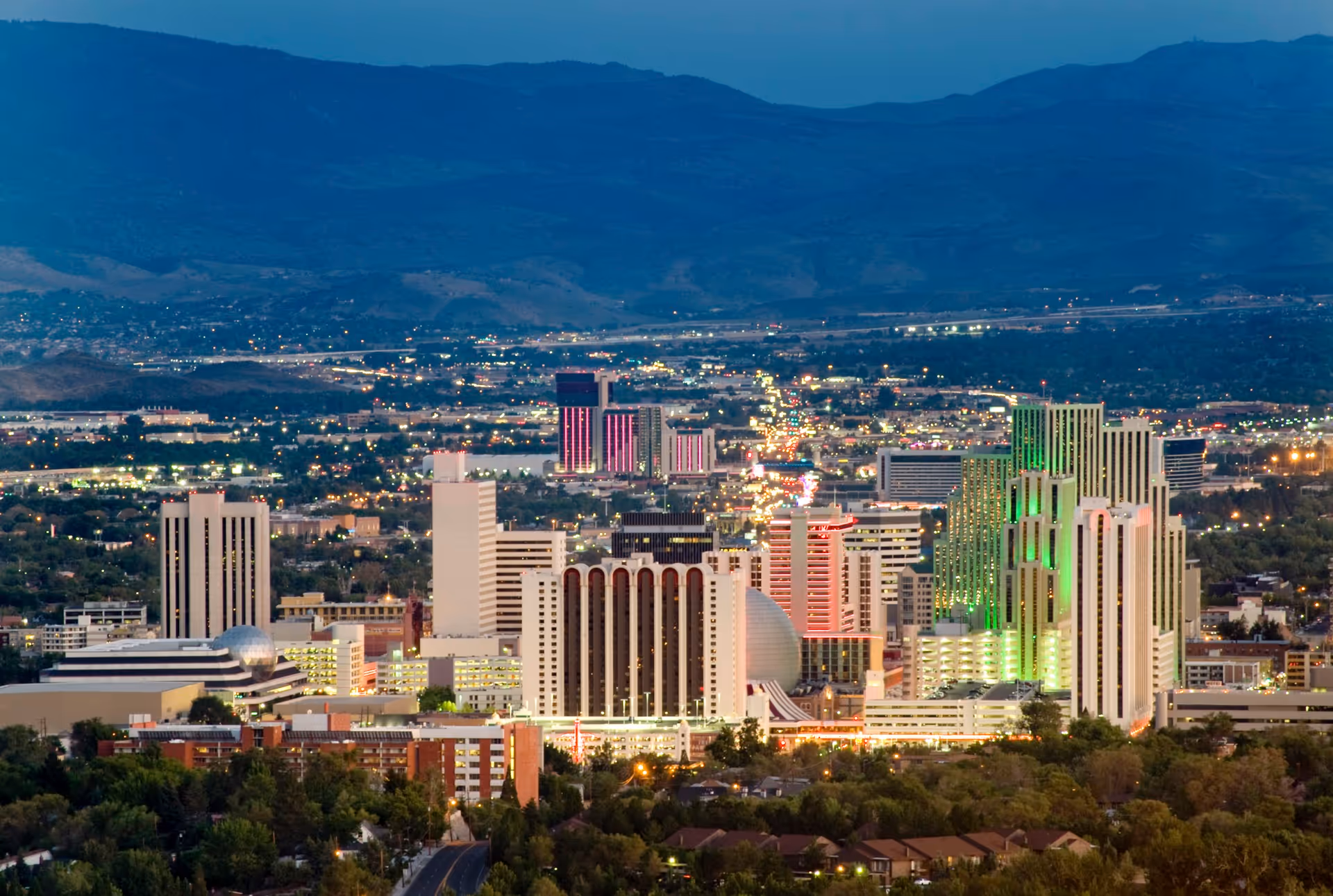 City skyline at dusk with illuminated buildings and distant mountains