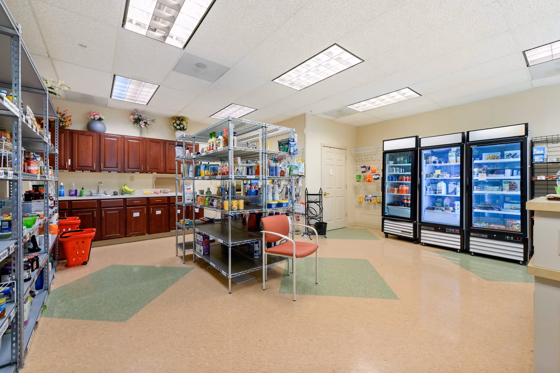 Well-lit institutional kitchen with metal shelves, cabinets, and multiple refrigerators.