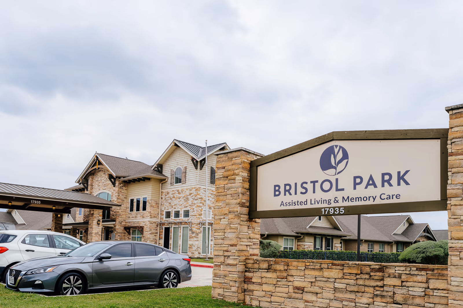 Front exterior of Bristol Park assisted living facility with a large sign and parked cars.