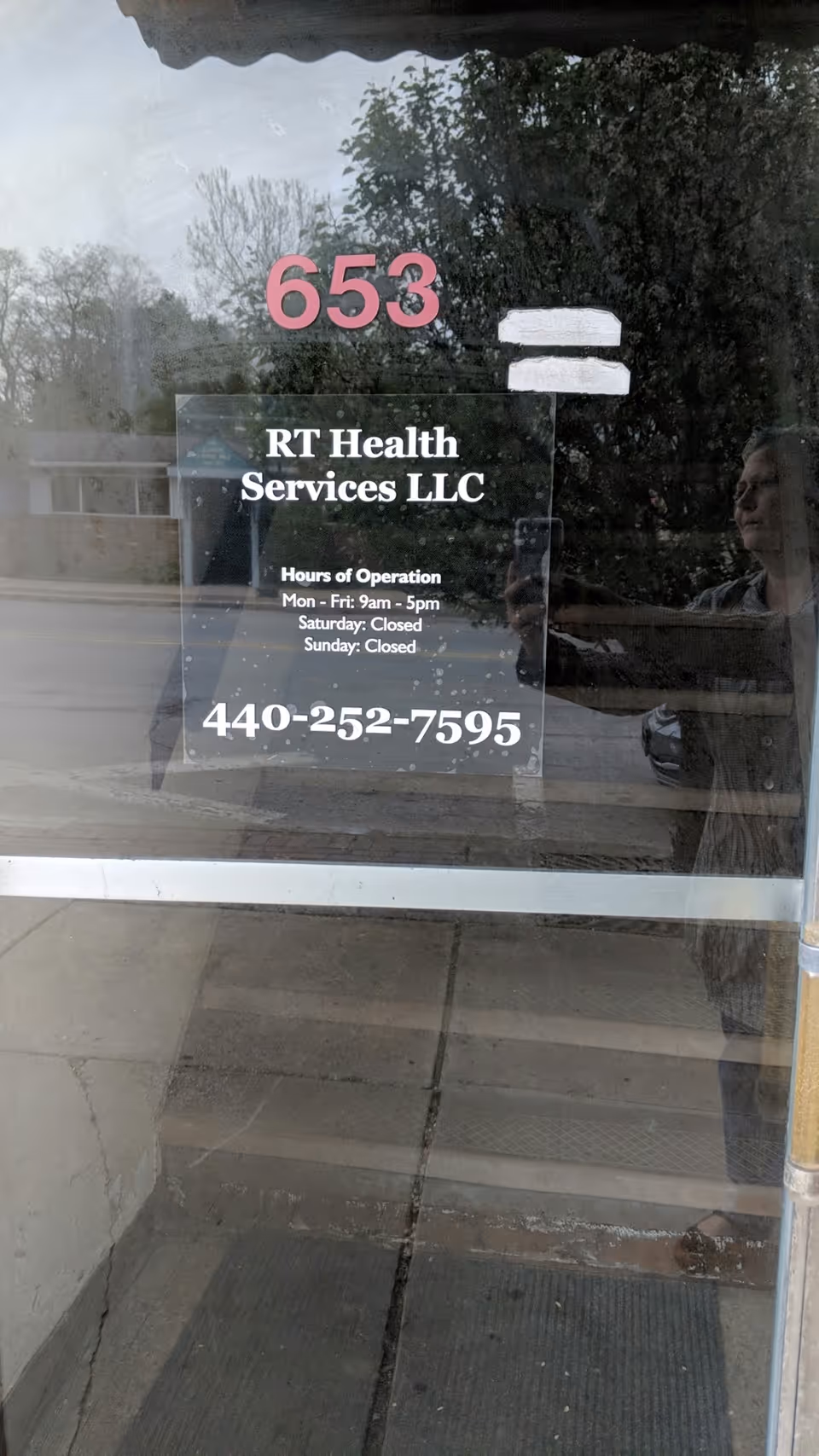 Glass entry door shows RT Health Services LLC sign and operation hours with reflections outside.