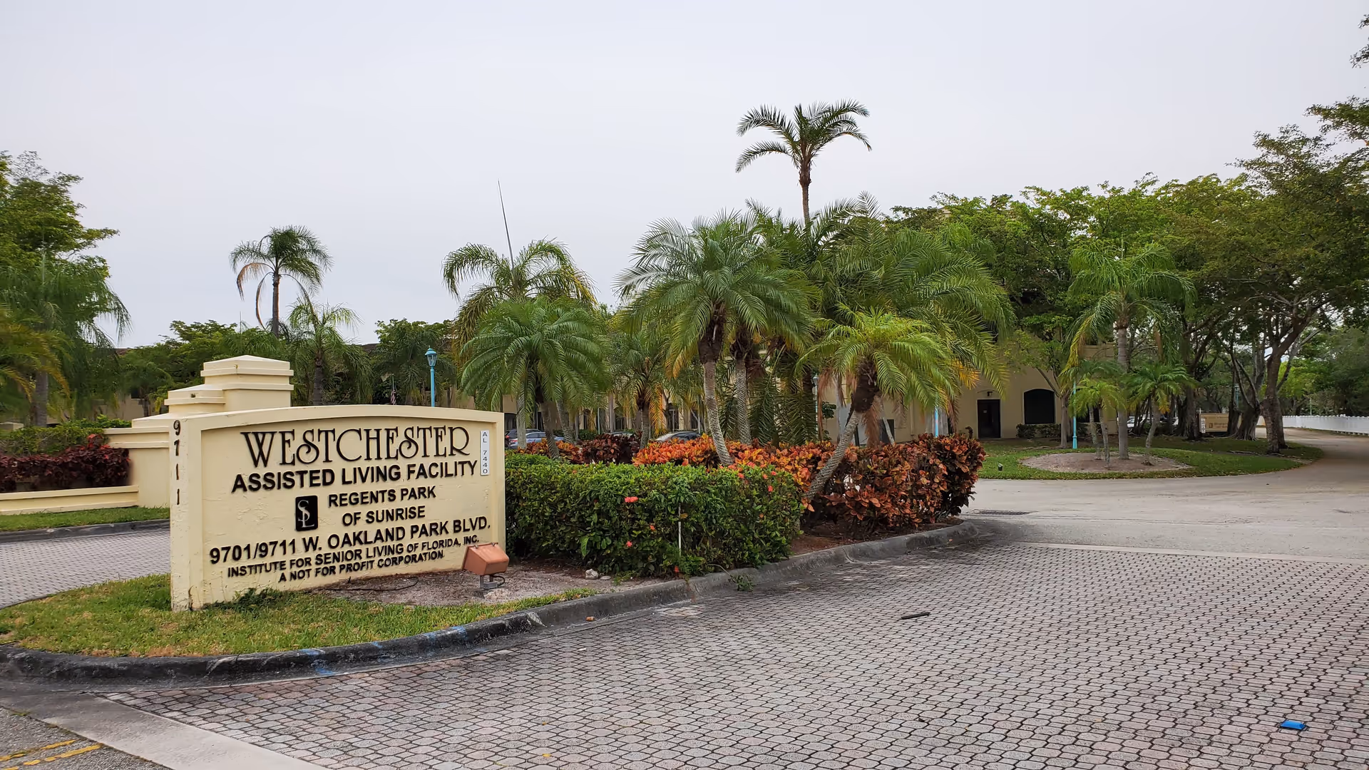 Exterior view of a senior living facility entrance with a large sign and palm trees.
